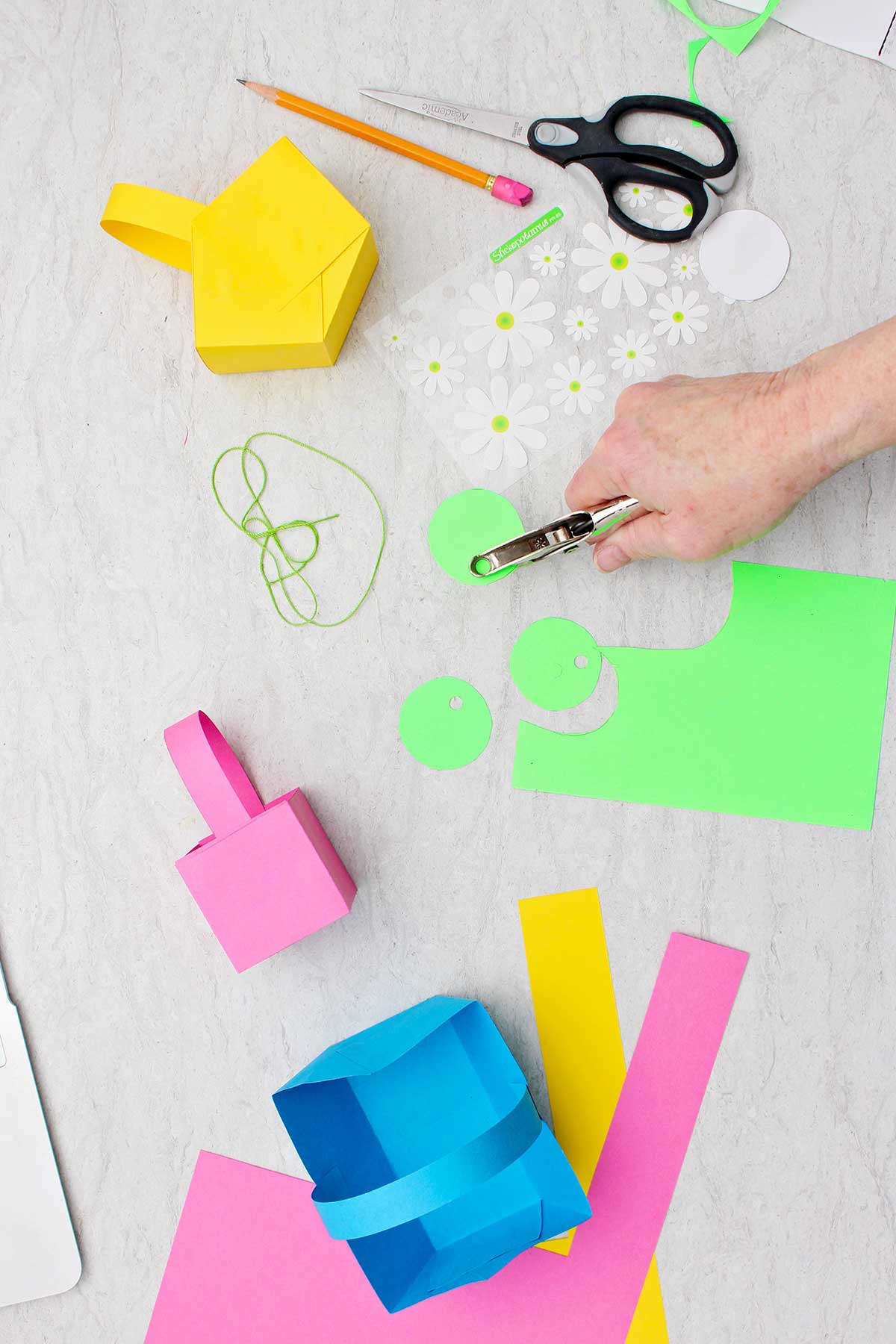Pessoa furando buracos em círculos cortados de papel verde para fazer etiquetas para as mini cestas de Páscoa.