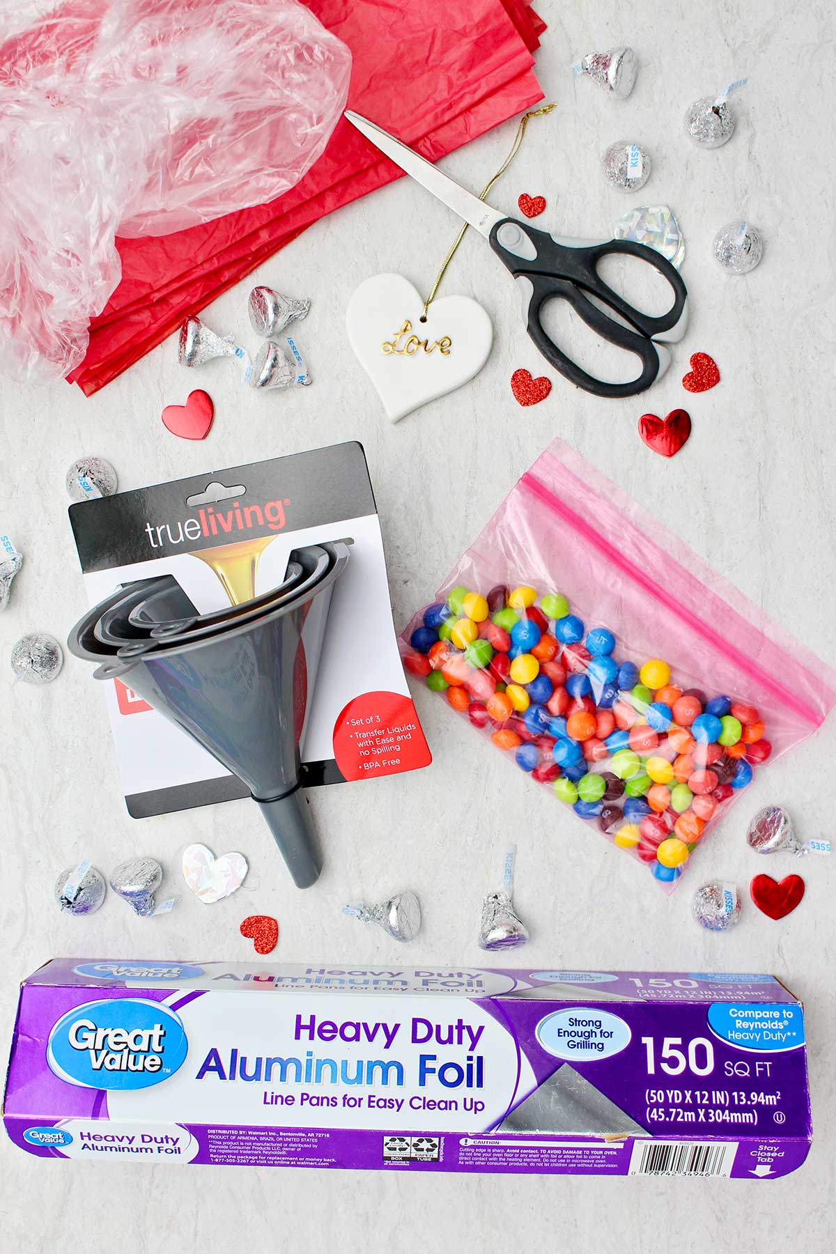 Materiais para fazer um gigante Beijo Hershey de Dia dos Namorados DIY. Funis plásticos, saco de doces, tesoura, papel alumínio e outros pequenos Beijos Hershey.