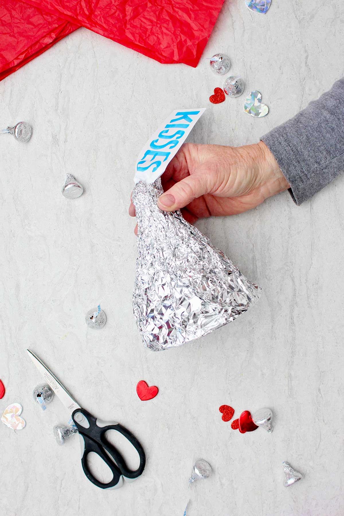 Pessoa segurando um Beijo Gigante de Hershey DIY concluído com tesoura, decorações de coração e beijos espalhados ao redor.