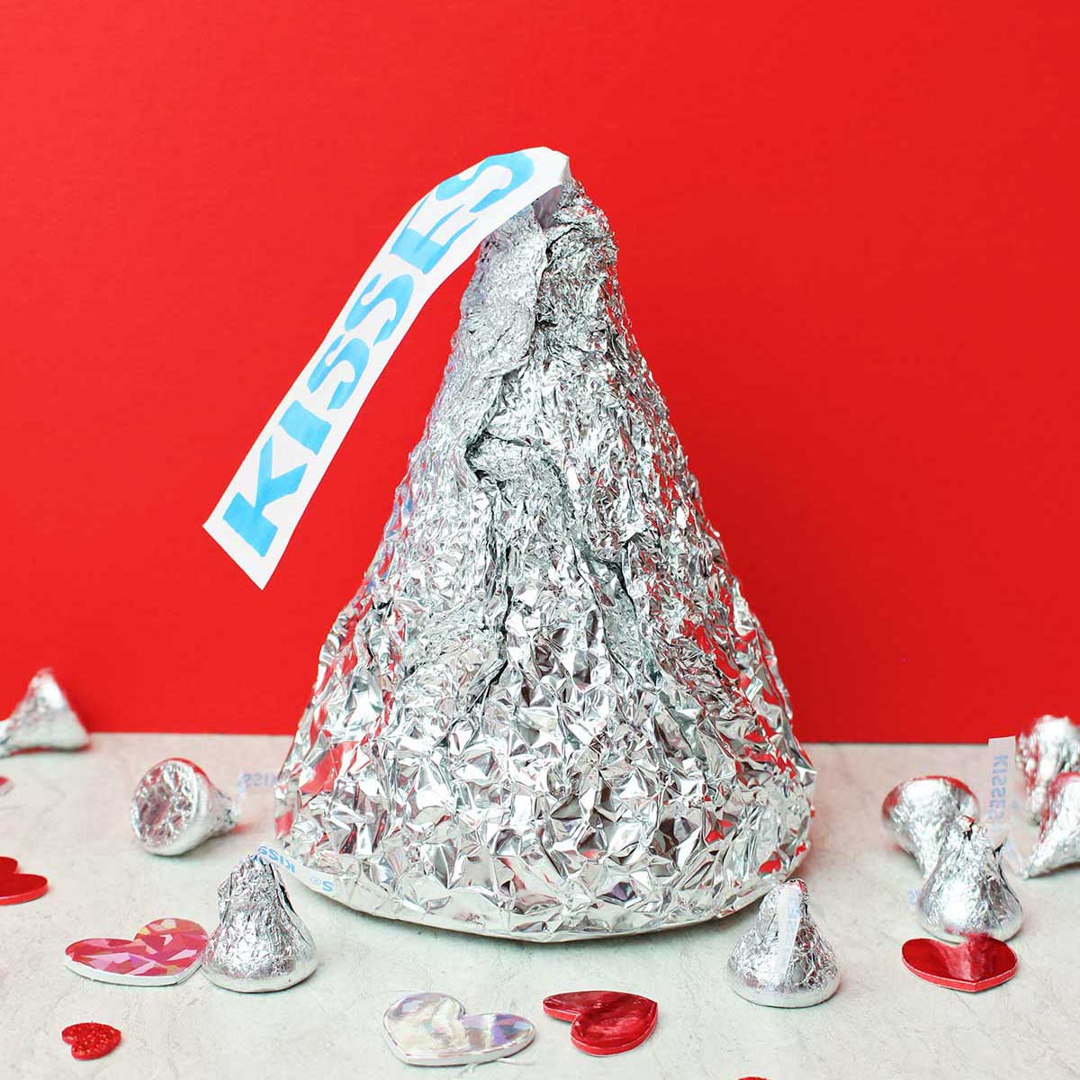 Giant Hershey Kiss com beijos de tamanho real e decorações de coração contra um fundo vermelho.
