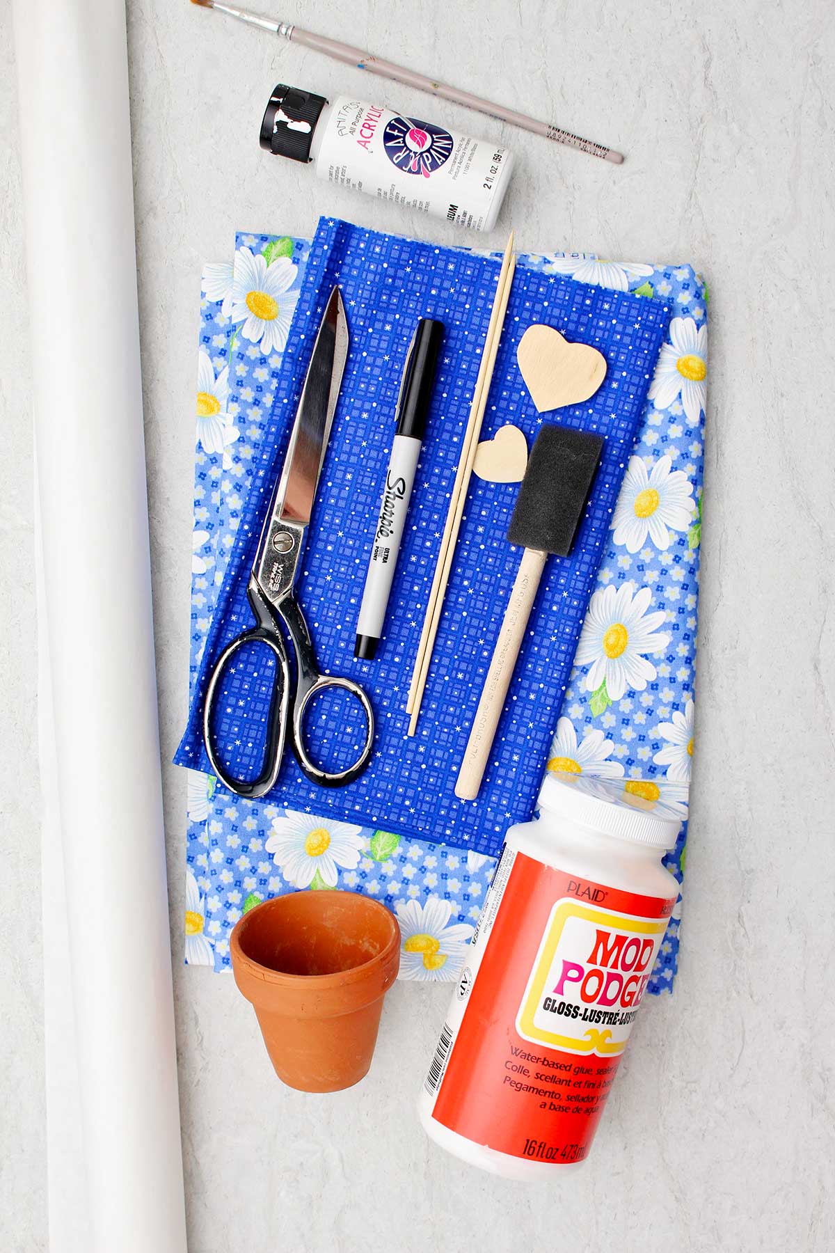Mod podge, tecido, um vaso de flores, tesouras, um marcador e outros suprimentos para fazer um vaso de flores decoupado com tecido.