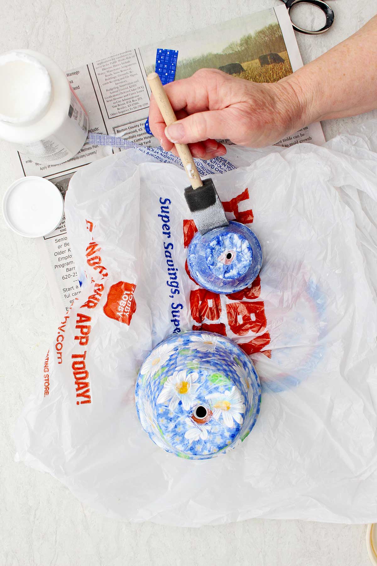 Uma pessoa pintando mod podge em um vaso menor com outro vaso maior secando ao lado.