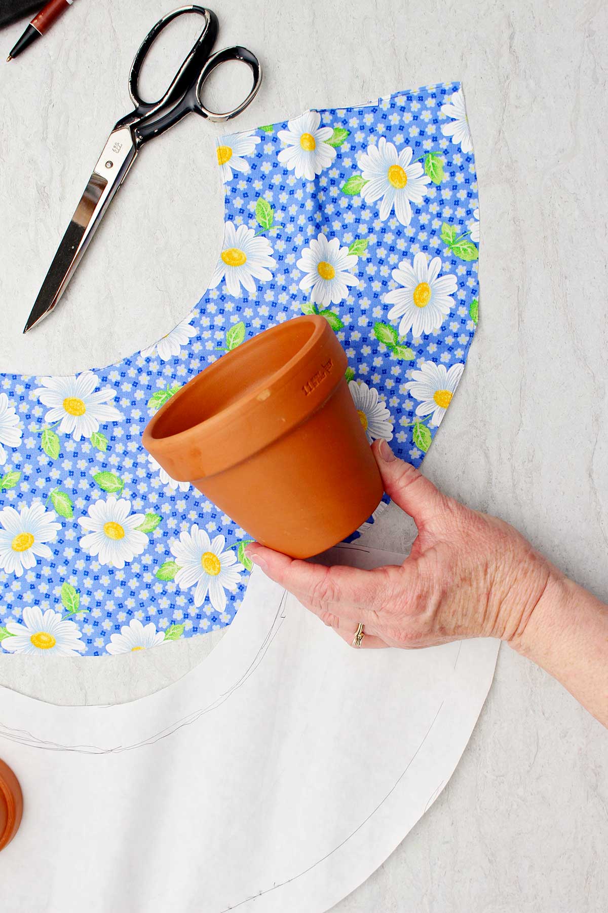 Uma pessoa segurando um pequeno vaso de flores com pedaços de tecido cortados ao redor.