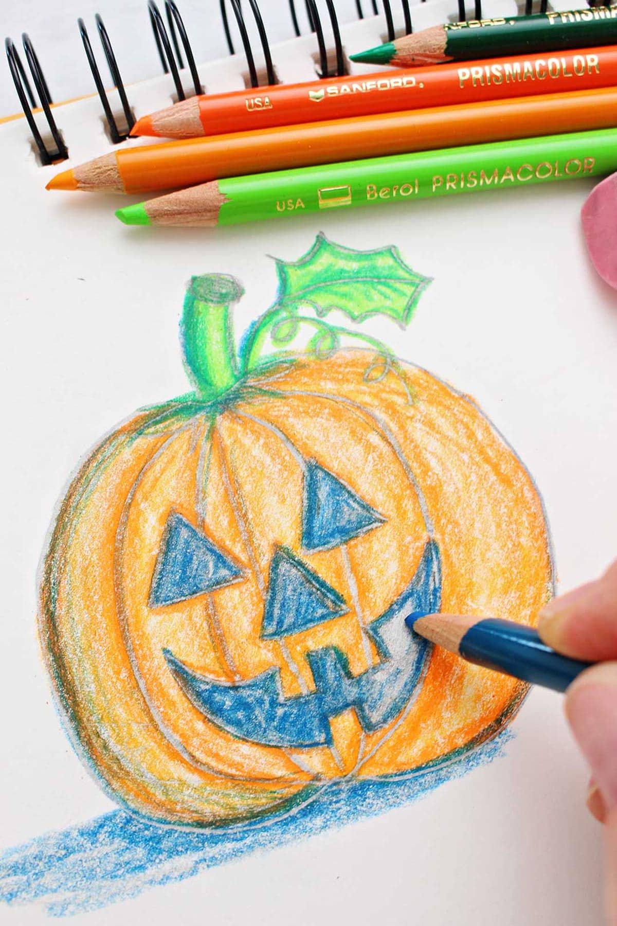 Mão preenchendo a boca de um desenho de jack-o-lantern com lápis de cor.