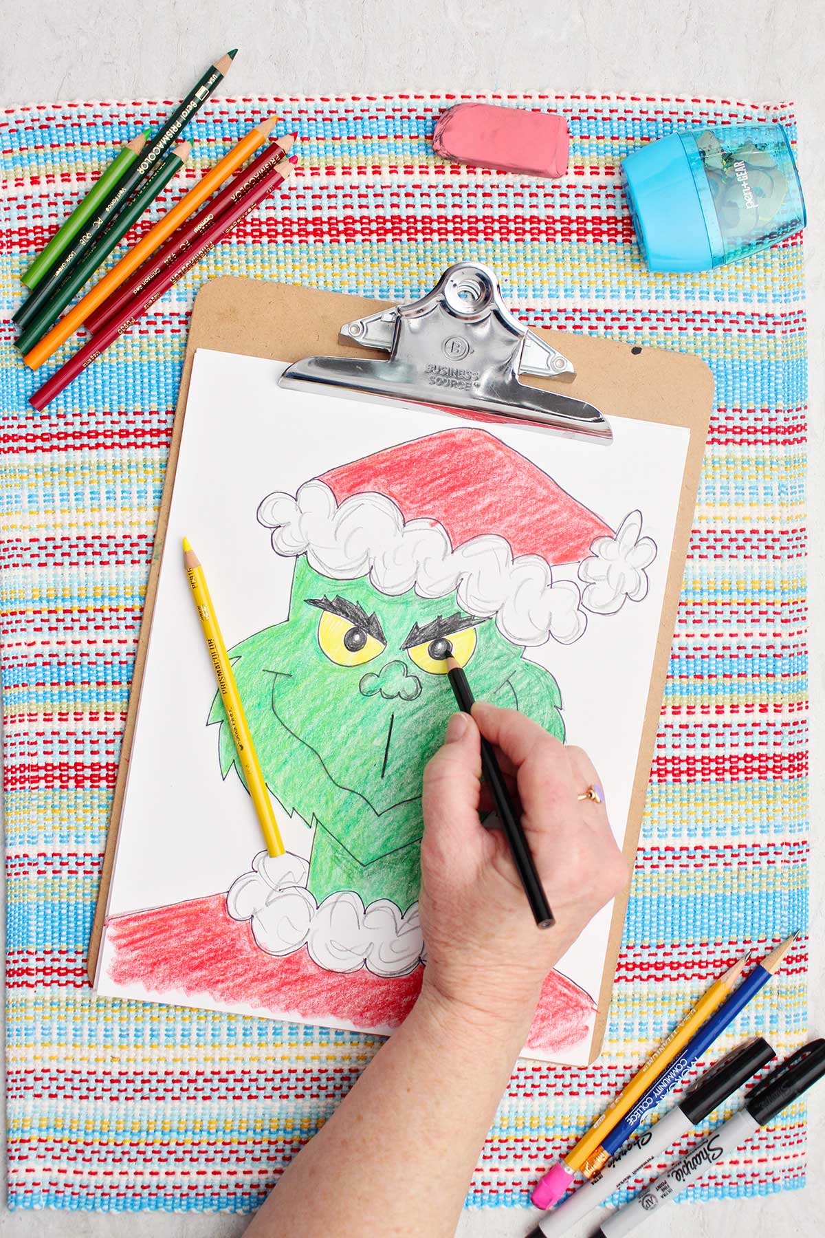 Pessoa colorindo as pupilas do Grinch de preto em uma versão colorida de um esboço do Grinch.