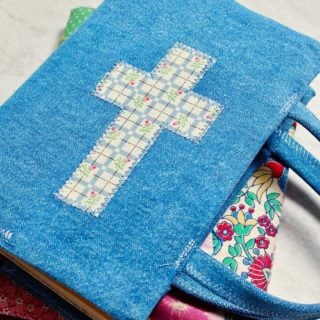 Duas capas de livro de tecido finalizadas, uma com tecido colorido de patchwork e outra com denim e uma cruz de tecido.