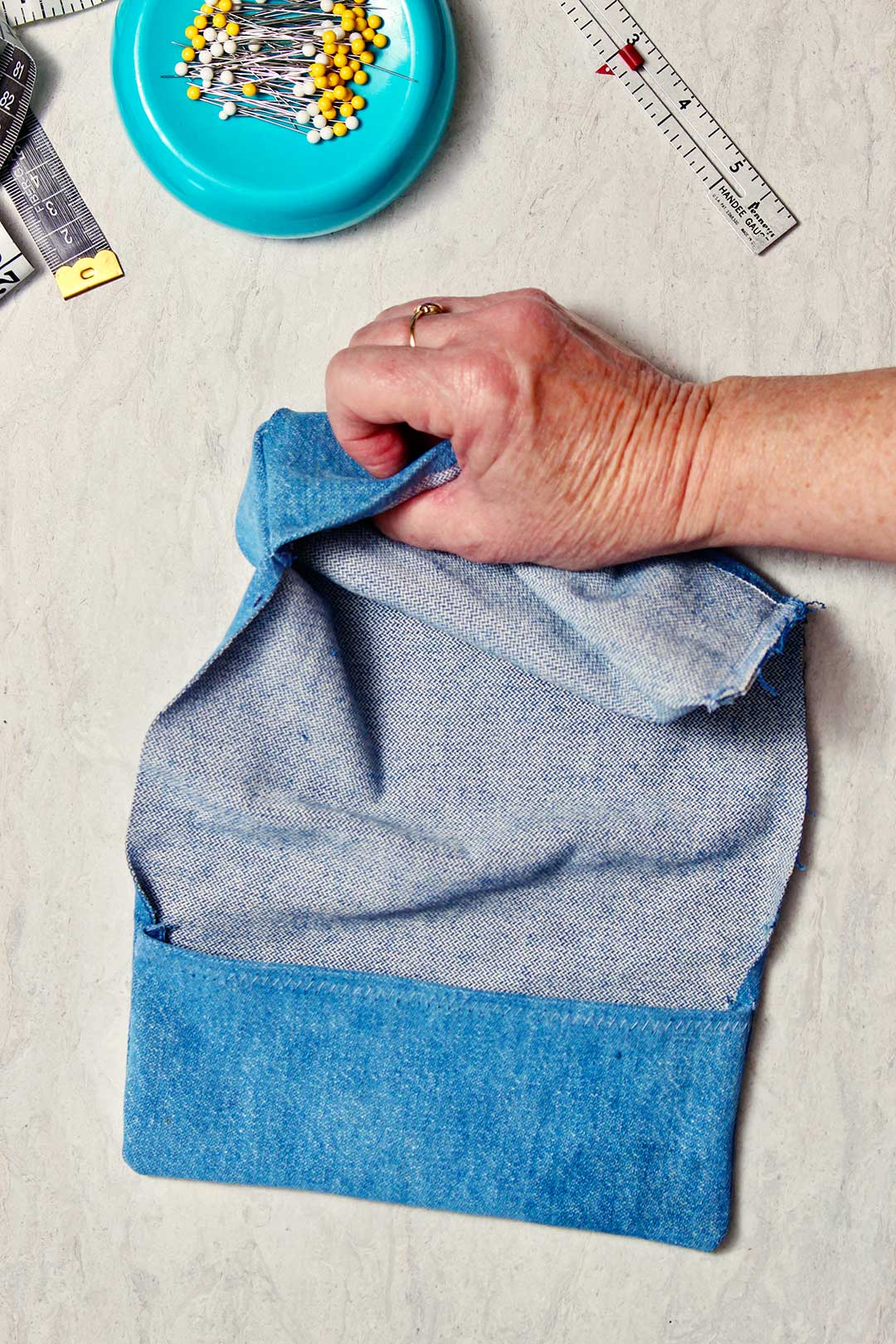 Uma mão virando o tecido de denim para o lado avesso.