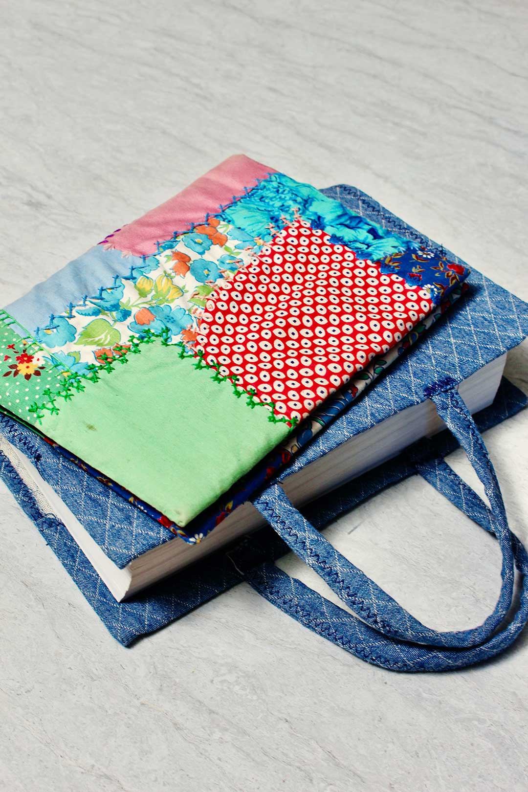Duas capas de livro de tecido finalizadas. Uma com um padrão colorido de patchwork e outra com tecido de denim.