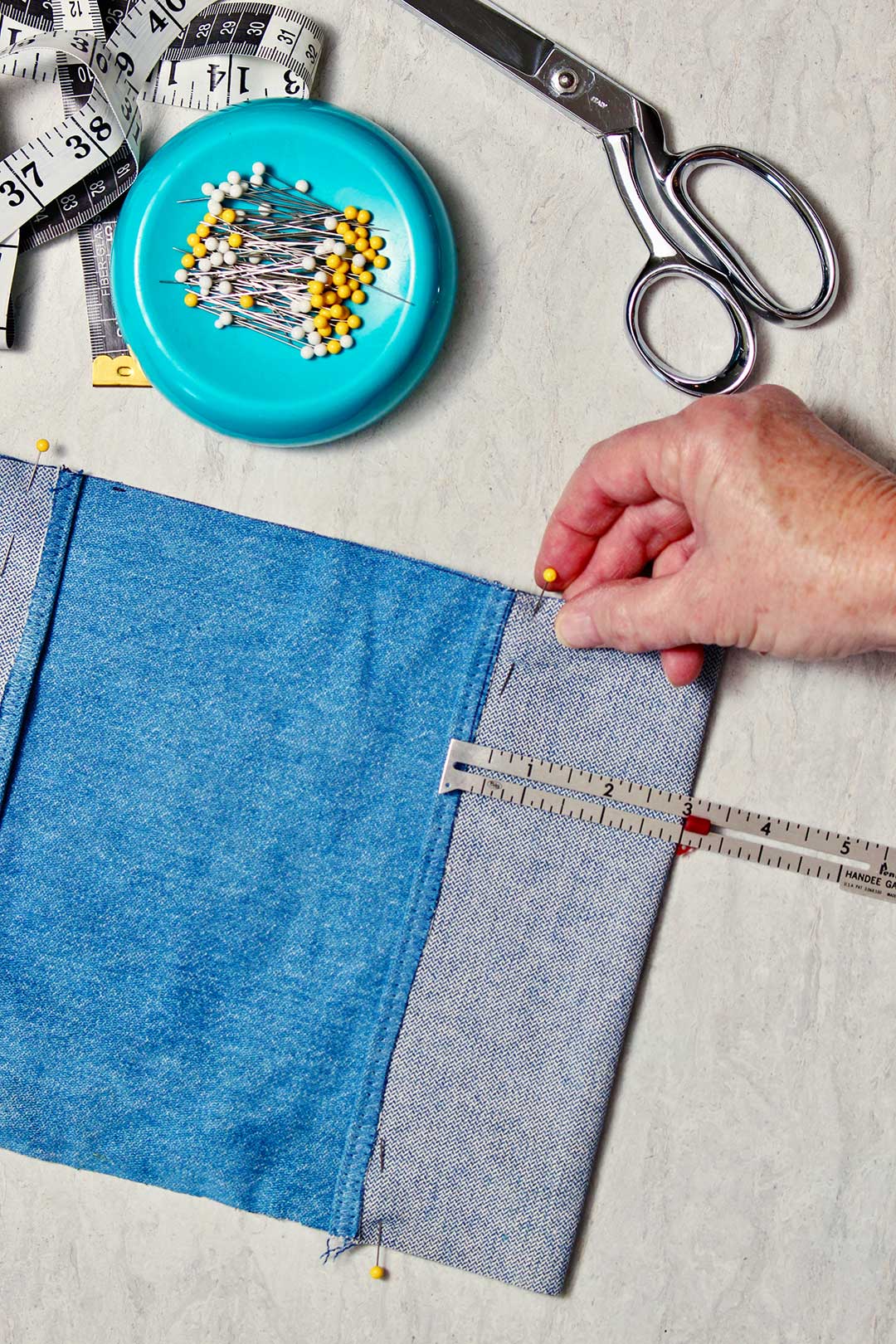 Uma régua pequena mede três polegadas no tecido de denim e está fixada para fazer uma aba para a capa.