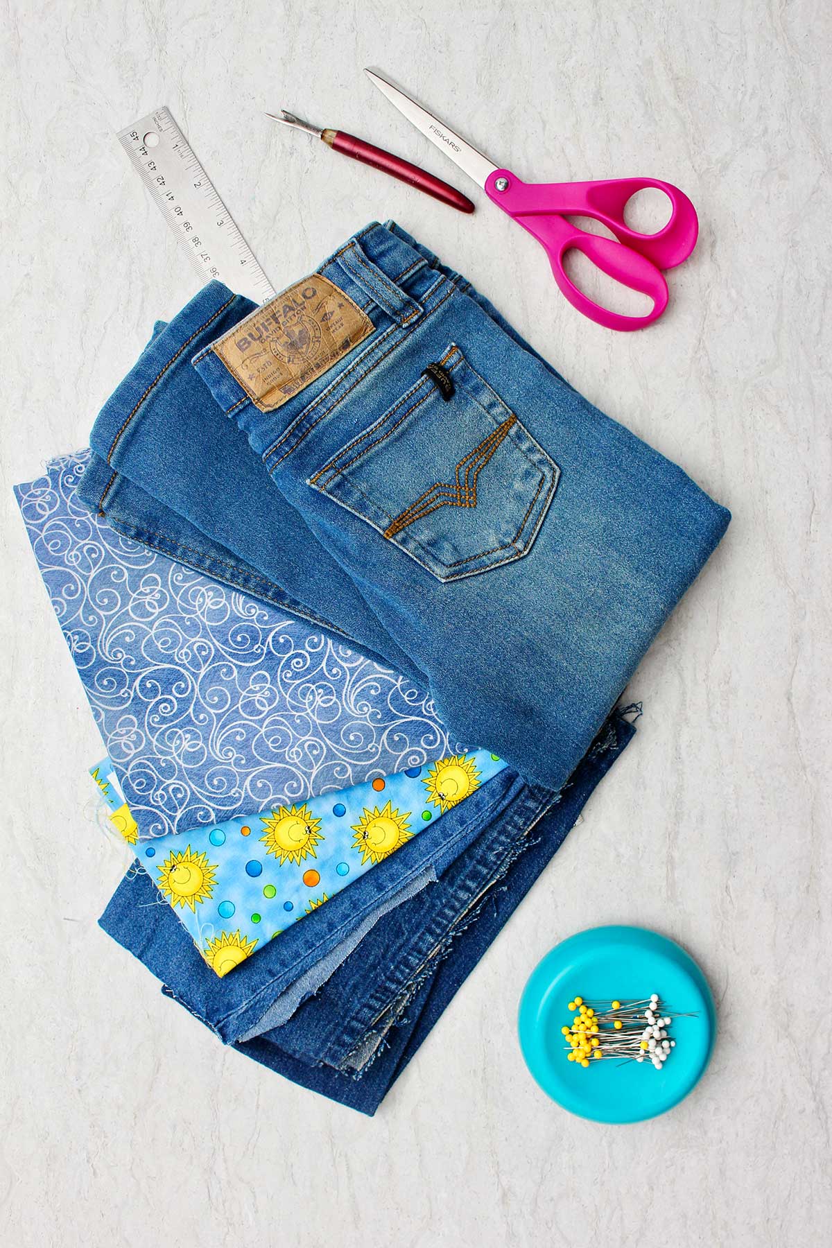 Materiais necessários para fazer jeans de barra sino: um par de jeans, tesouras, tecido decorativo, régua e alfinetes.