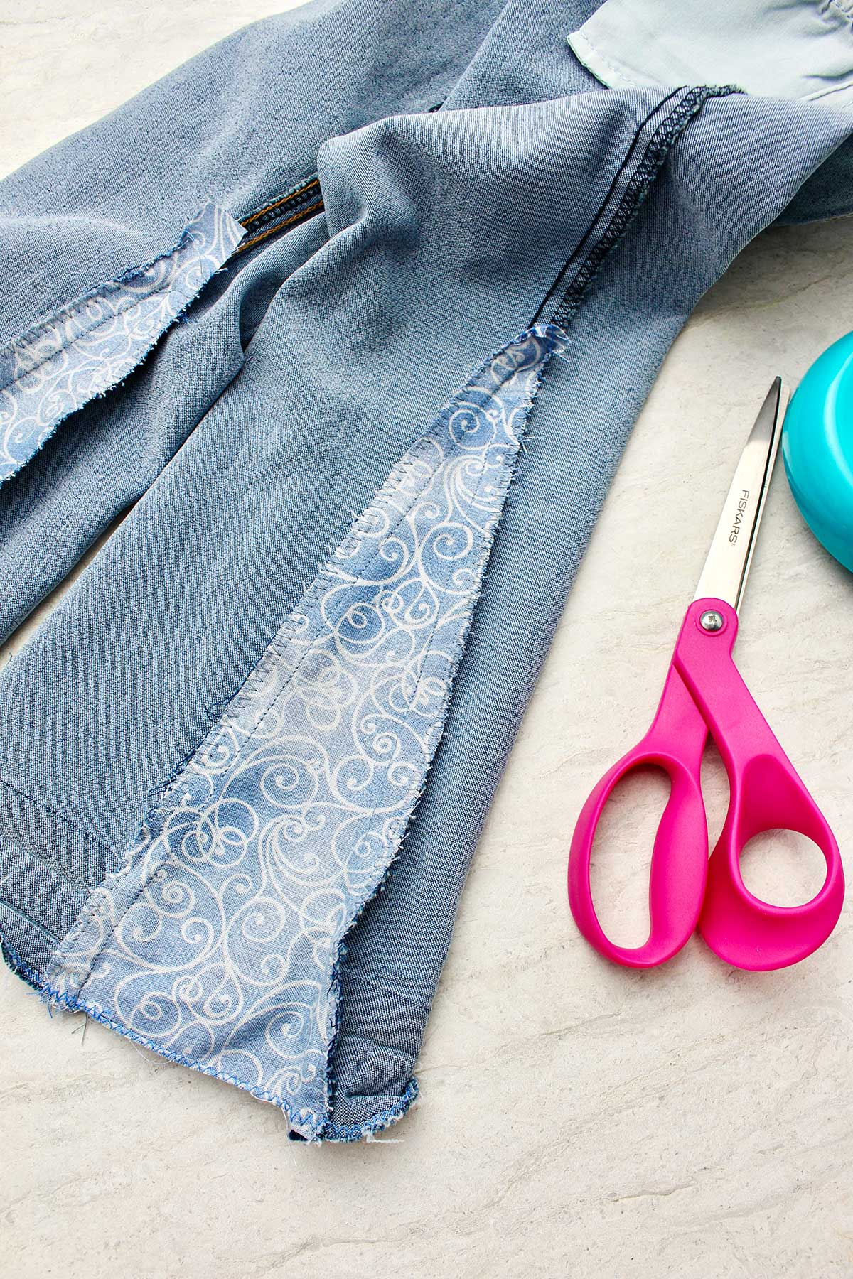 Close da parte de dentro de um jeans do avesso com um pedaço de tecido costurado junto, com tesouras por perto.