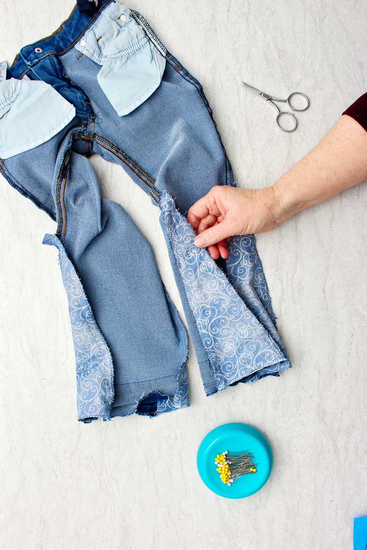 Mão mostrando jeans do avesso com um pedaço de tecido costurado para fazer barra sino.