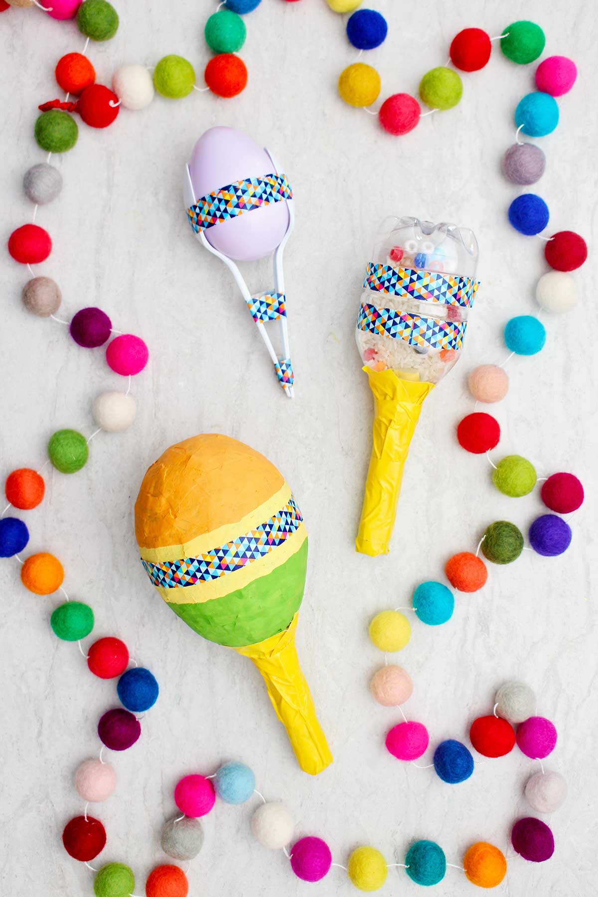 Três maracas completas diferentes com pompons coloridos ao lado.