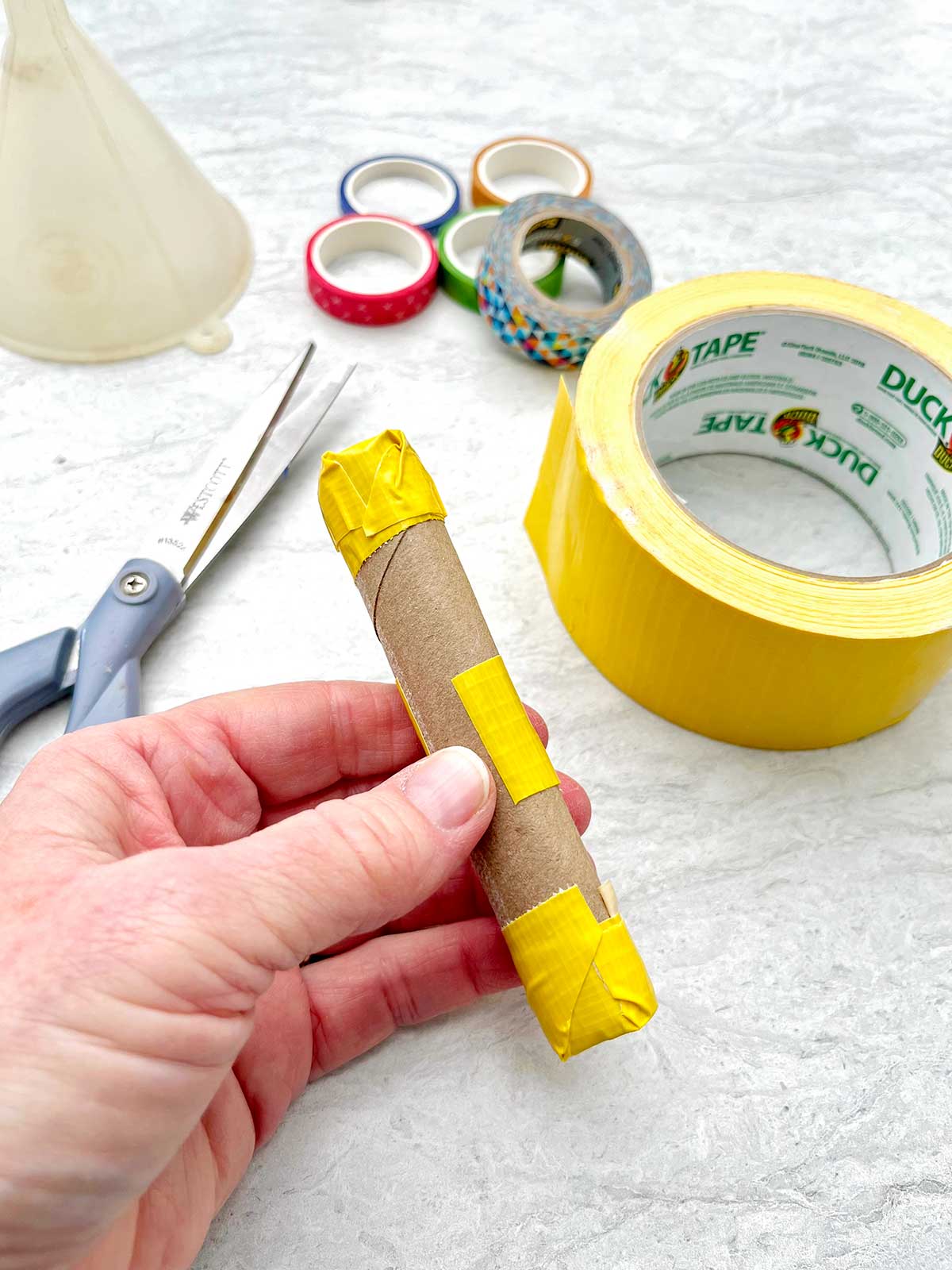 Pessoa mostrando como segurar um rolo de papel toalha junto para fazer um cabo de maraca.