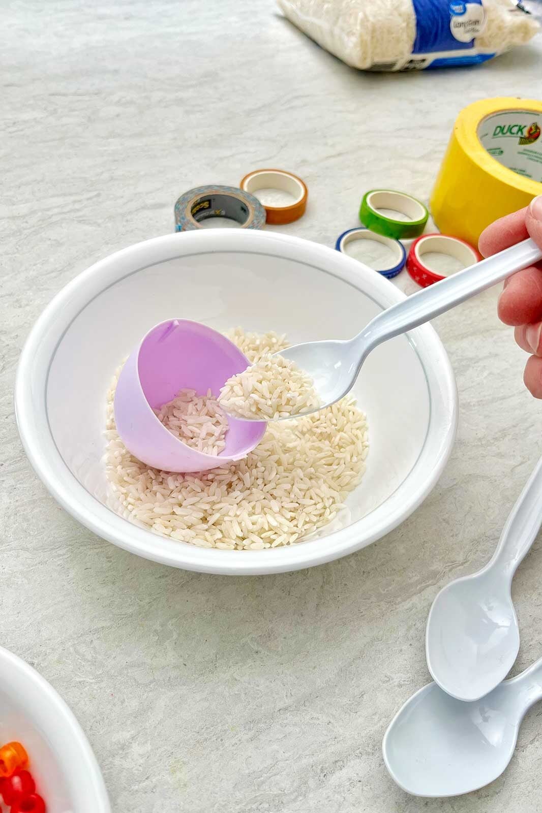 Pessoa preenchendo um ovo de plástico roxo com arroz.