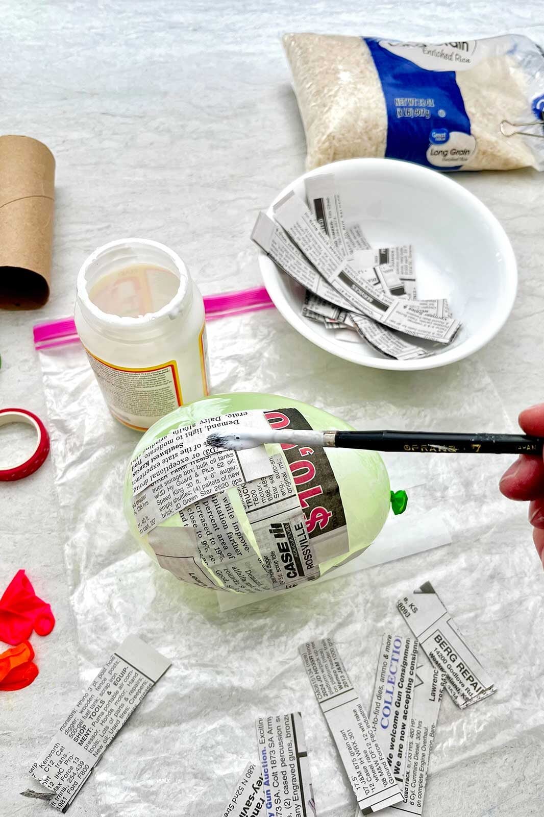 Pessoa pintando tiras de papel de jornal em um balão com mod podge.