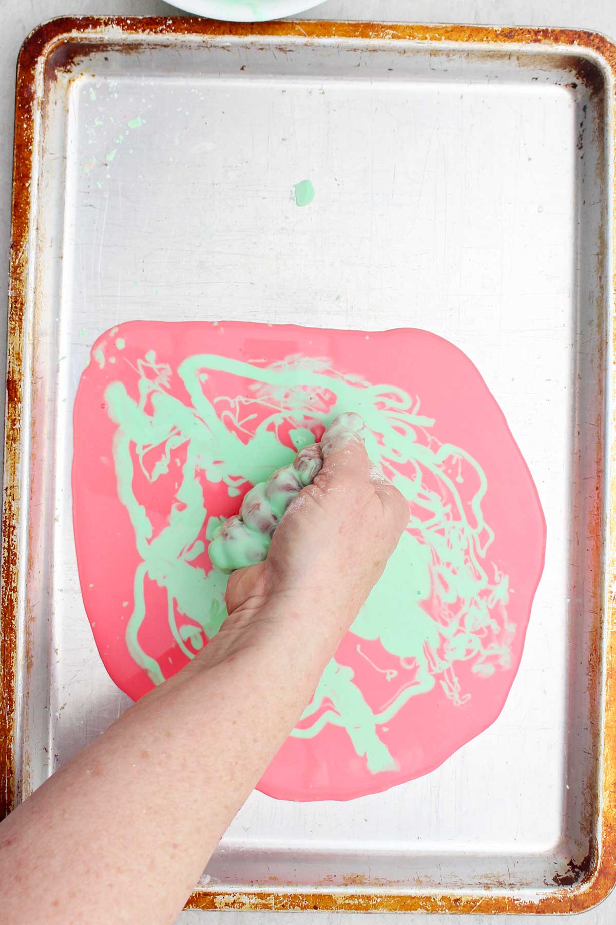 Uma pessoa apertando um punhado de oobleck sobre uma assadeira.