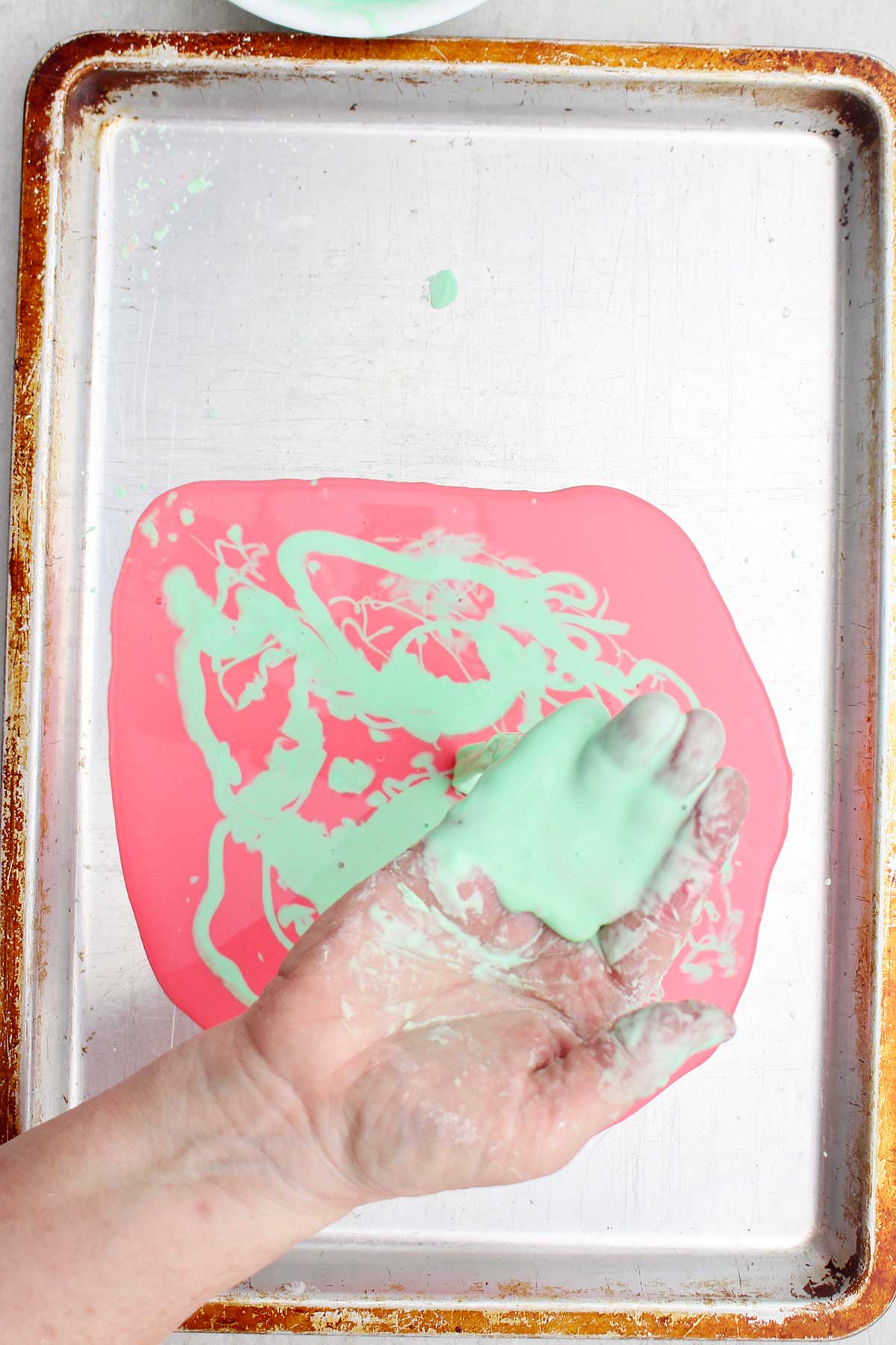 Uma pessoa segurando um punhado de oobleck verde claro sobre uma assadeira.