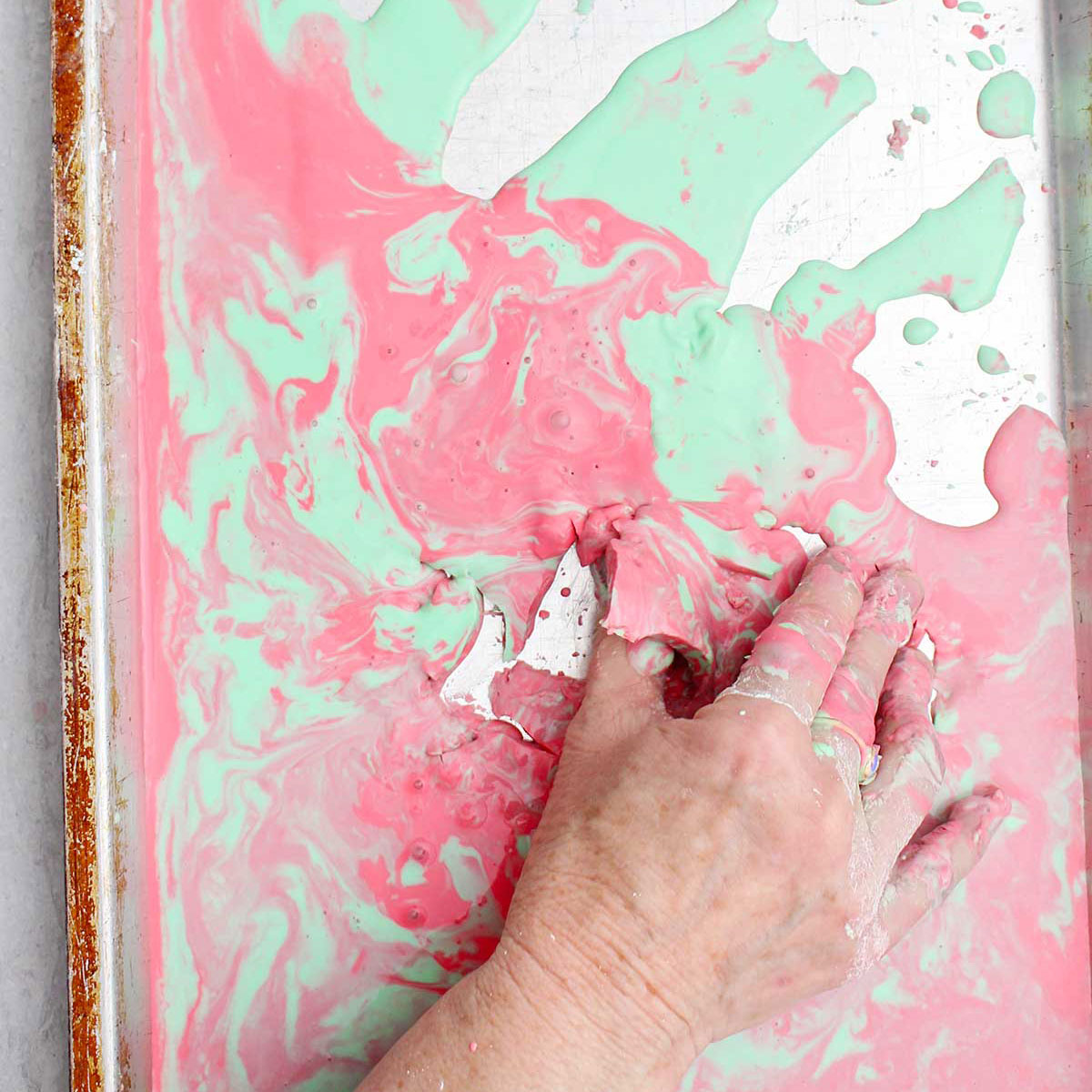 Uma pessoa pegando um pedaço semissólido de oobleck rosa e verde de uma assadeira.