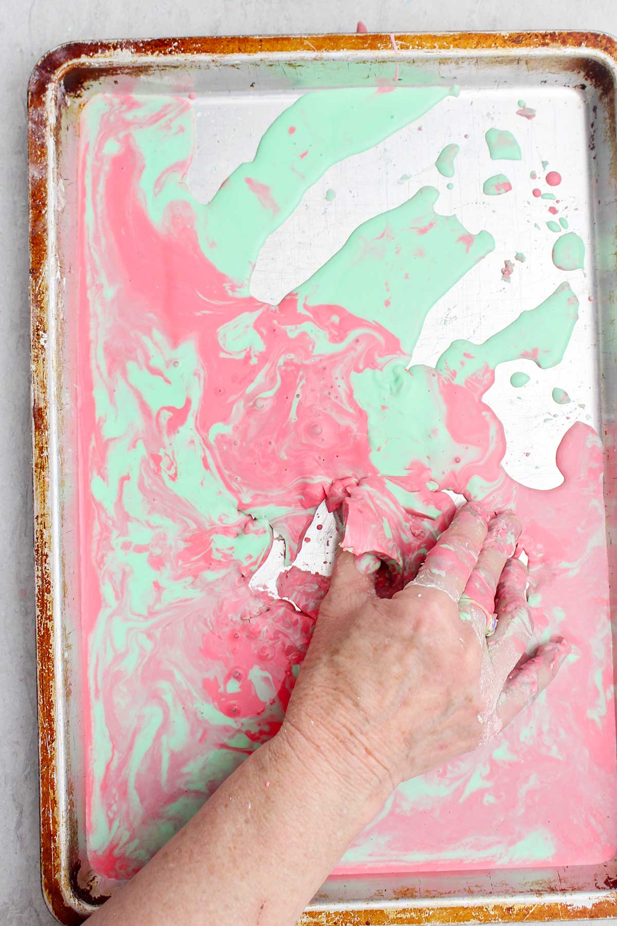 Uma pessoa pegando um pedaço semi sólido de oobleck rosa e verde de uma assadeira.
