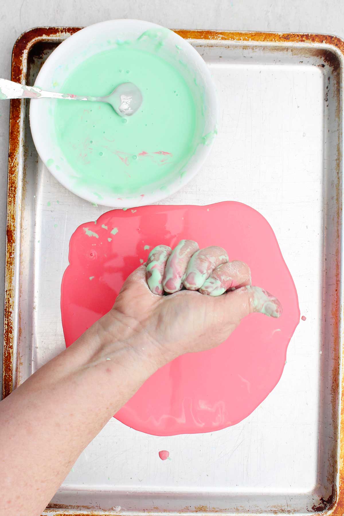 Uma pessoa apertando um punhado de oobleck sobre uma assadeira.