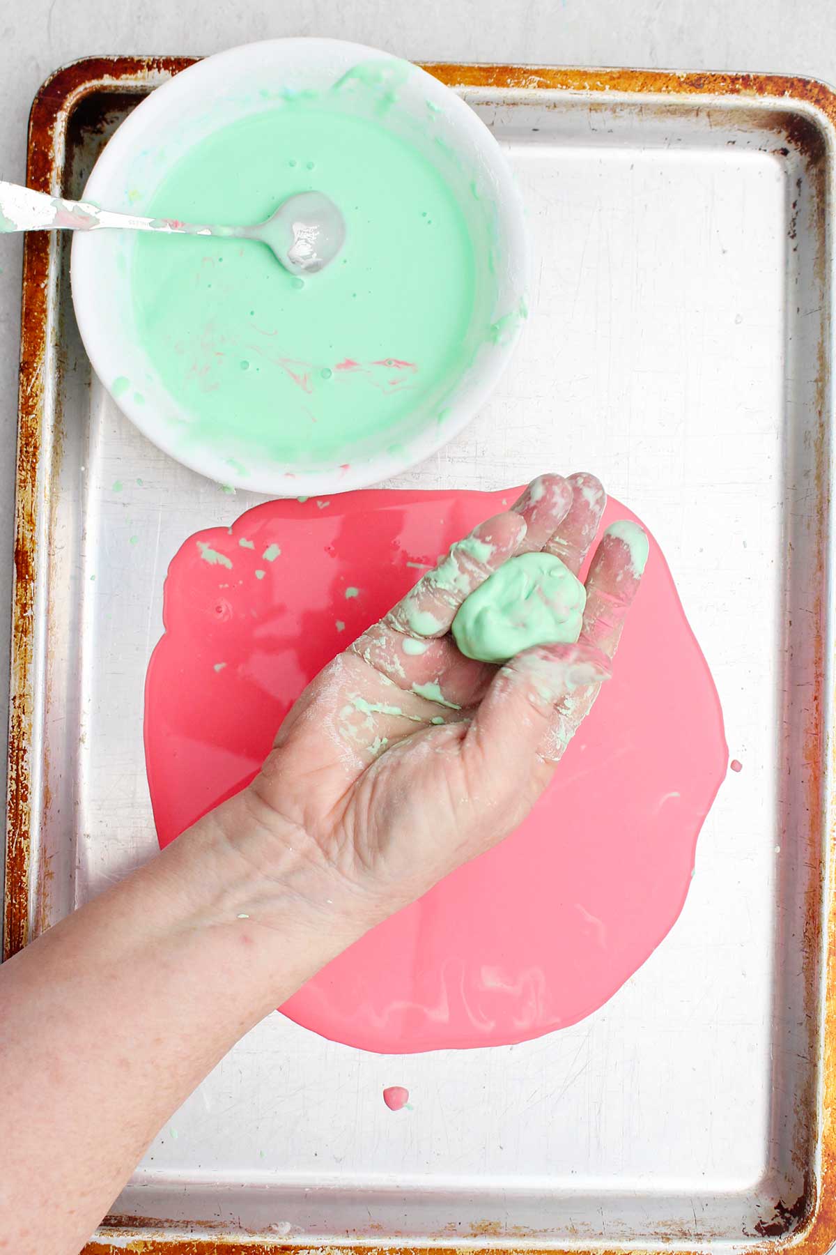 Uma pessoa mostrando uma bola de oobleck verde claro sobre uma assadeira.