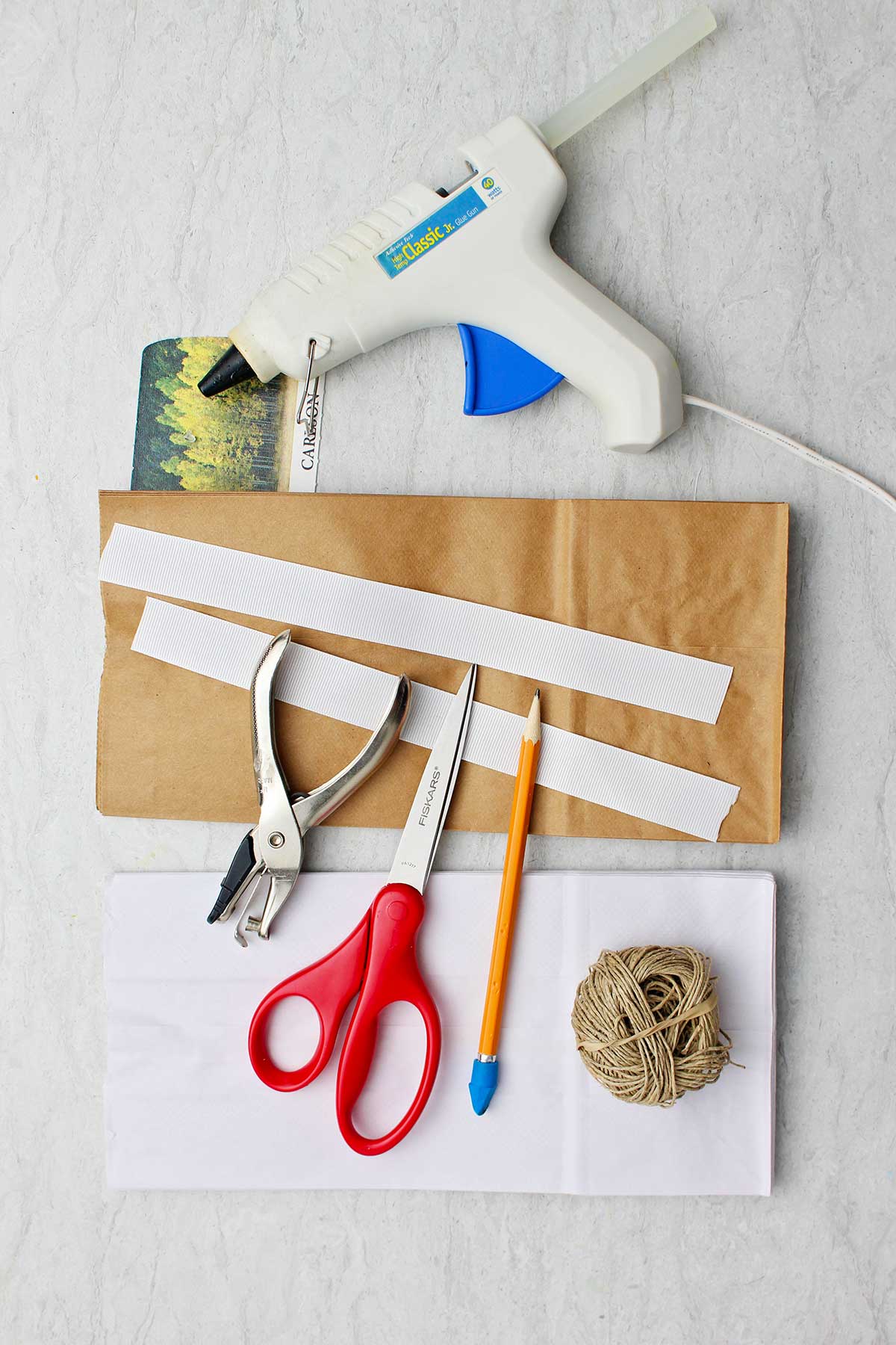 Materiais para fazer flocos de neve de papel. Fita, cola quente, perfurador, tesoura, lápis, barbante e sacos de papel.