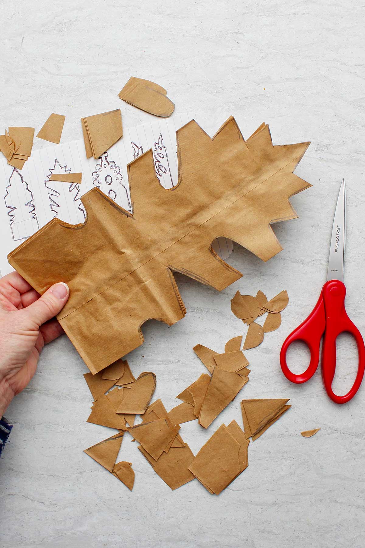 Mão segurando uma pilha de sacos de papel marrons dobrados após cortar o padrão.