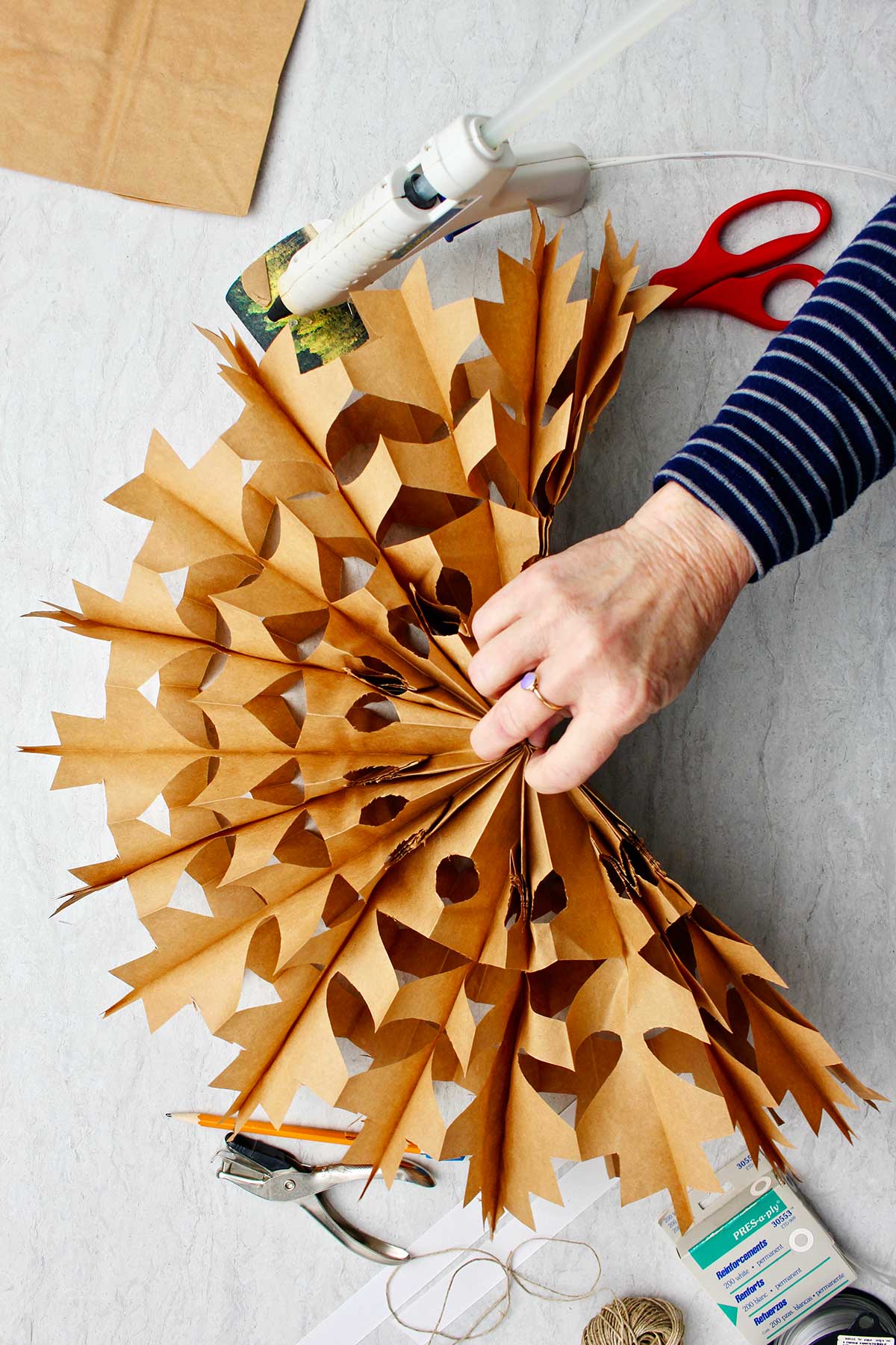 Mão desdobrando o floco de neve feito de saco de papel marrom.