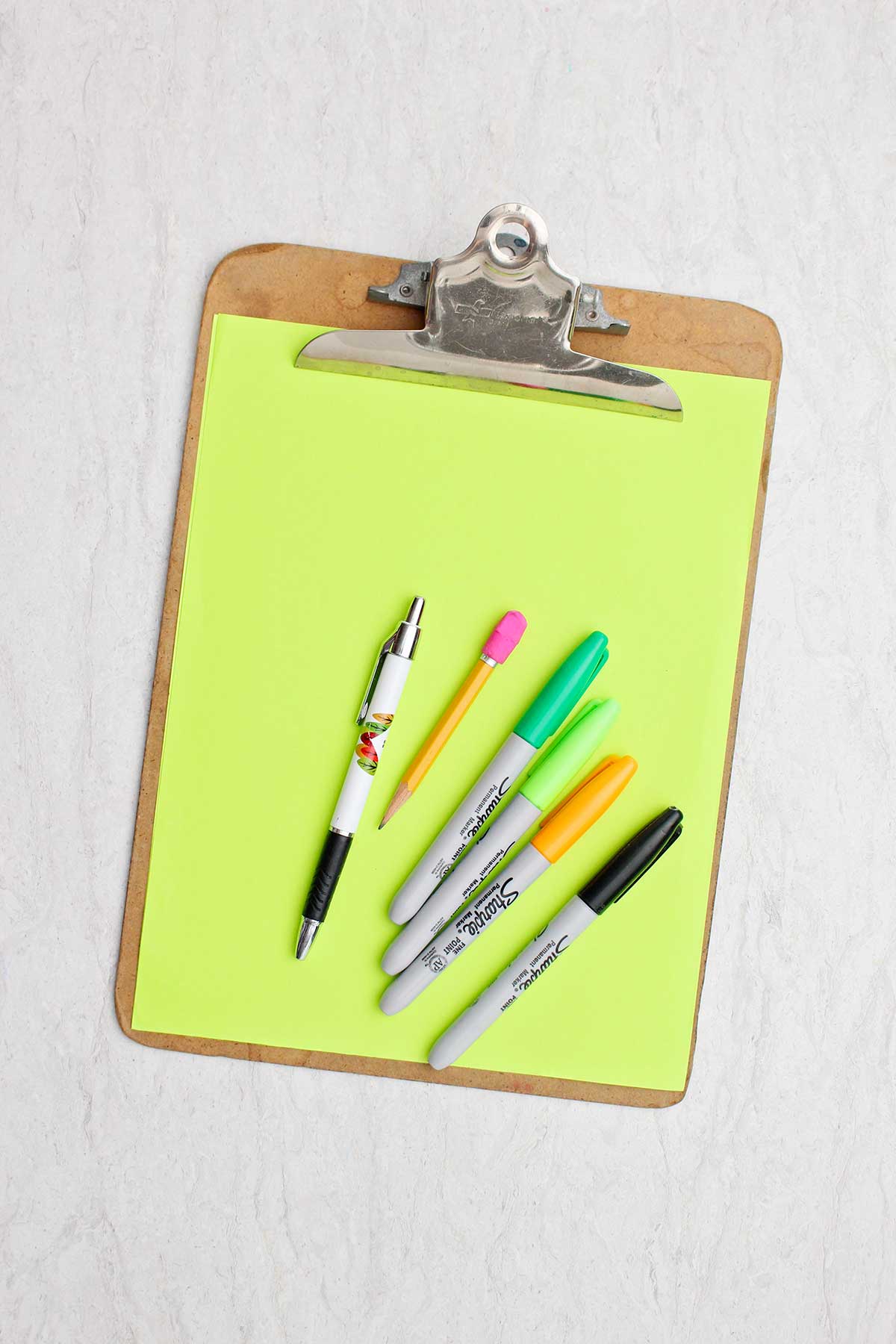 Um pedaço de papel verde, lápis, caneta e marcadores de diferentes cores.