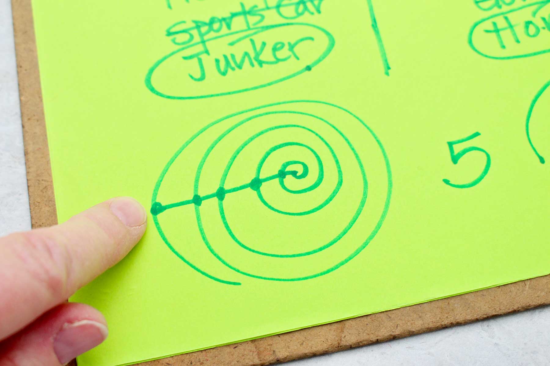 Uma pessoa mostrando o desenho de espiral e ponto que determina quantos números contar antes de riscar uma opção em um jogo MASH.