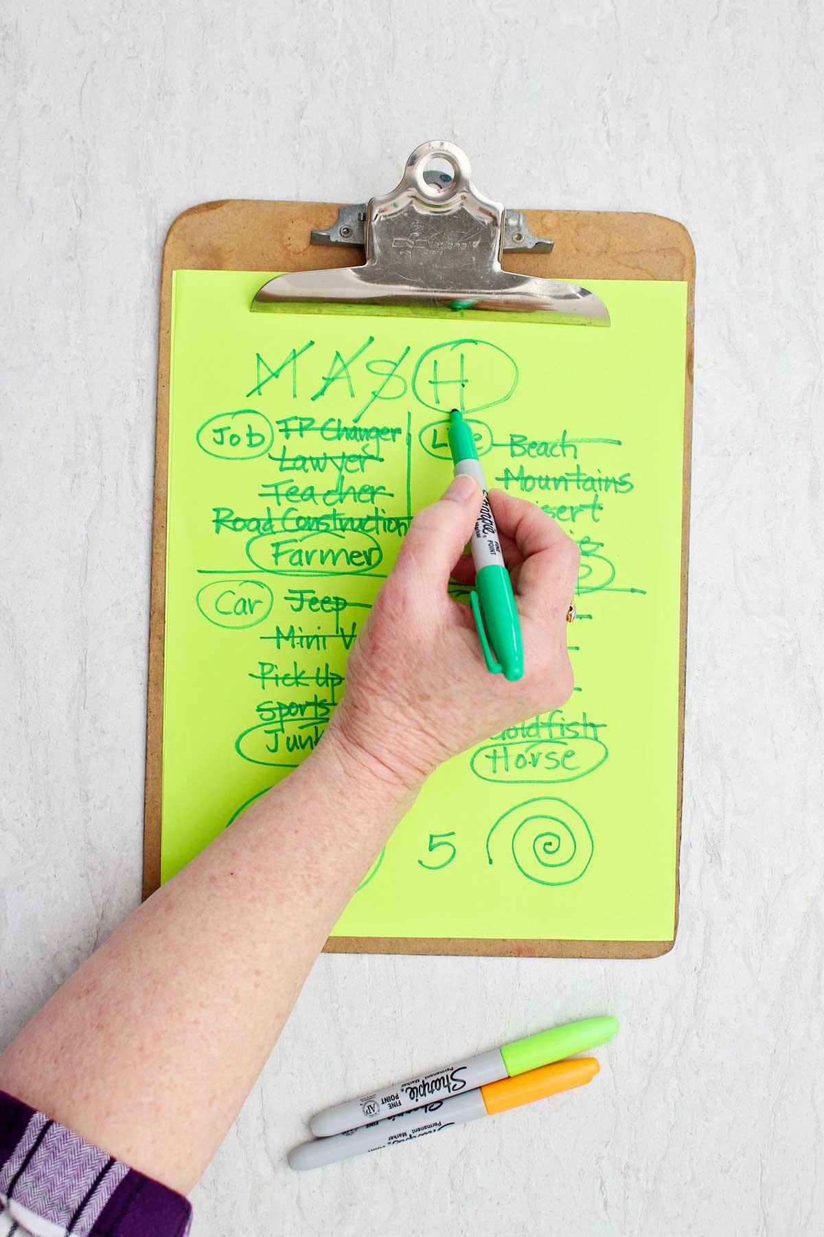 Uma pessoa circulando o "H" no mash com um marcador verde em um jogo de MASH.