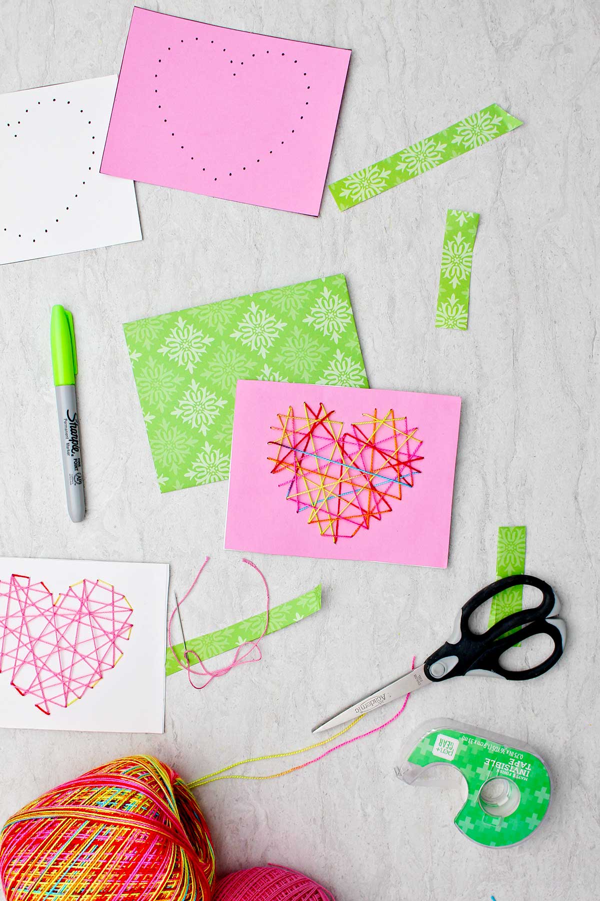 Dois cartões de dia dos namorados costurados feitos de papel rosa, branco e verde e fio multicolorido e dois outros cartões com furos prontos para serem costurados.
