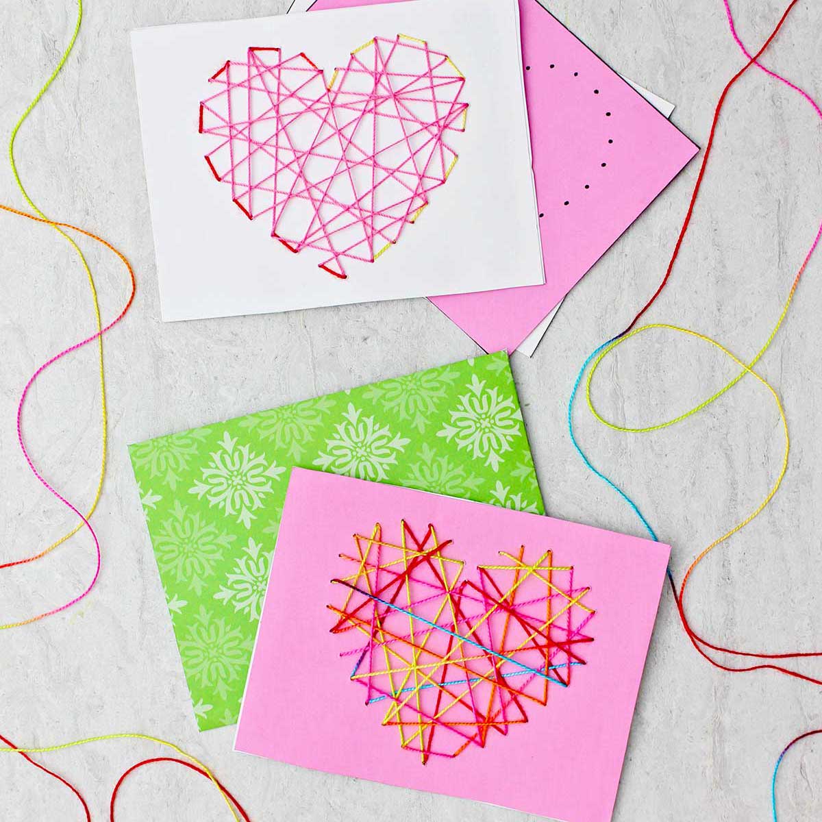 Dois cartões de dia dos namorados costurados feitos de papel rosa, branco e verde e fio multicolorido.