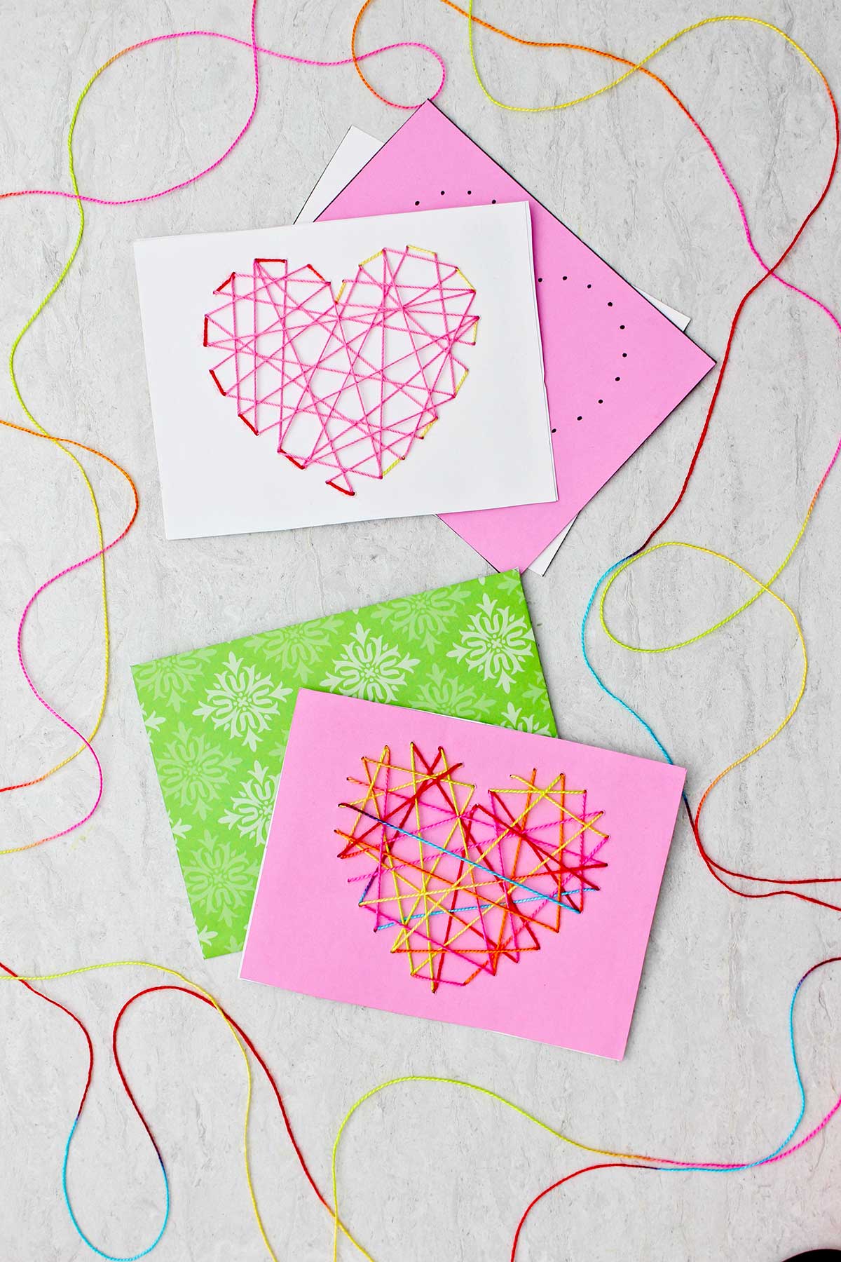 Dois cartões de Dia dos Namorados costurados feitos de papel rosa, branco e verde e linha colorida.