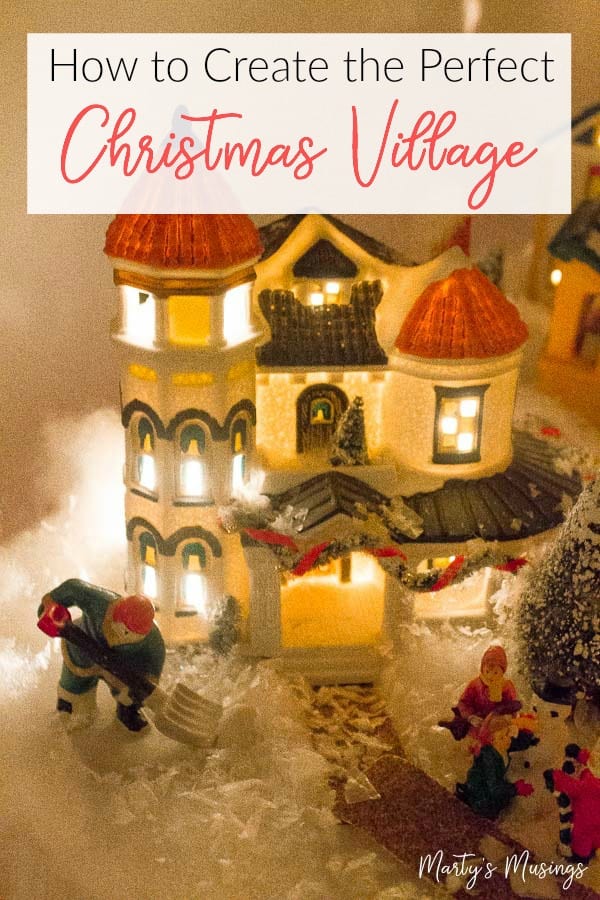 Casinha de vila de Natal em miniatura com pessoas na frente, iluminada à noite