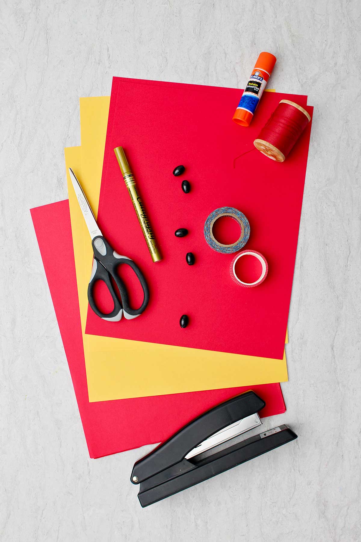 Materiais para fazer Lanternas Chinesas Simples. Papel vermelho e amarelo, tesoura, caneta dourada, fita, cordão, cola e grampeador.