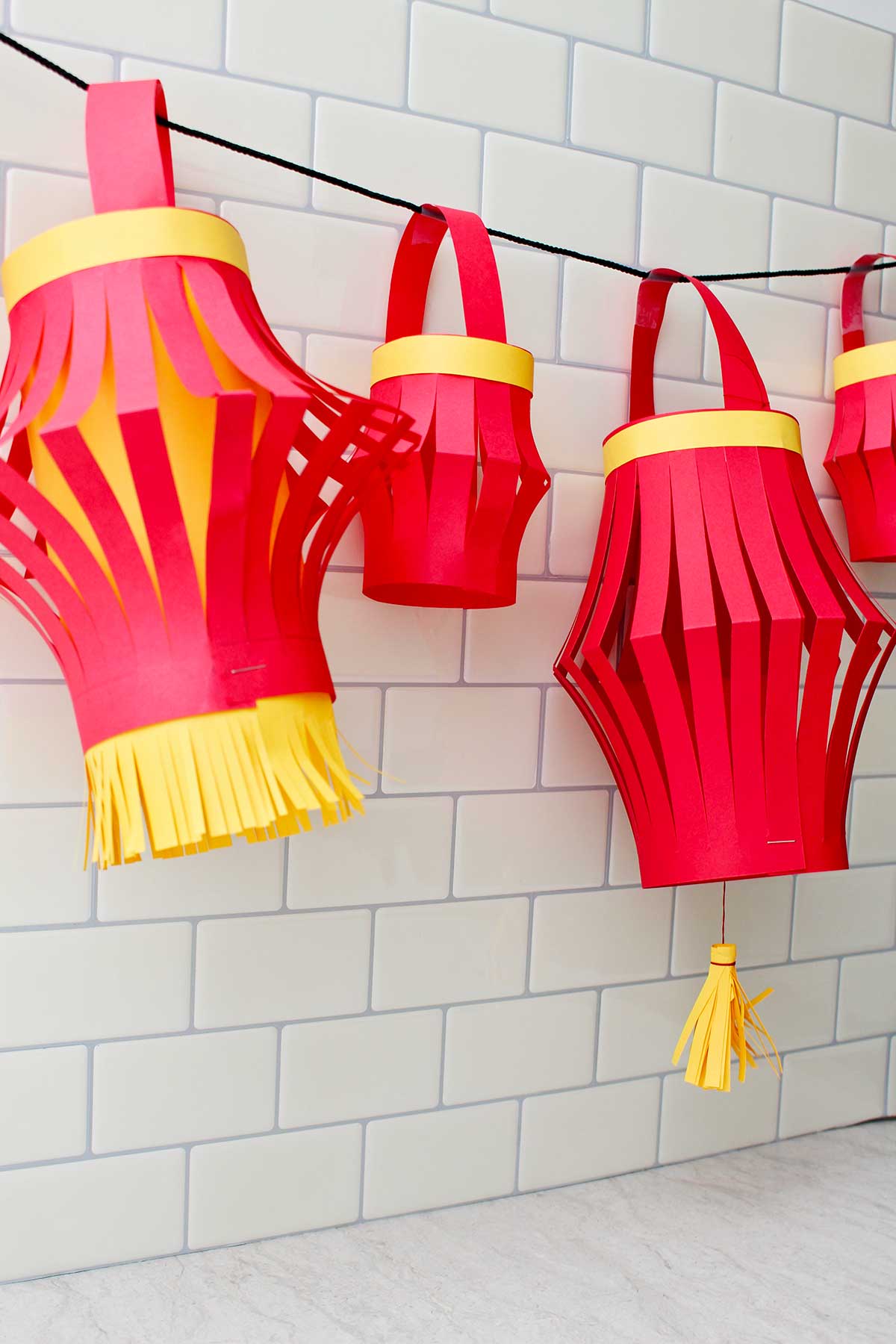 Quatro lanternas de papel completas penduradas contra um fundo de azulejos de metrô.