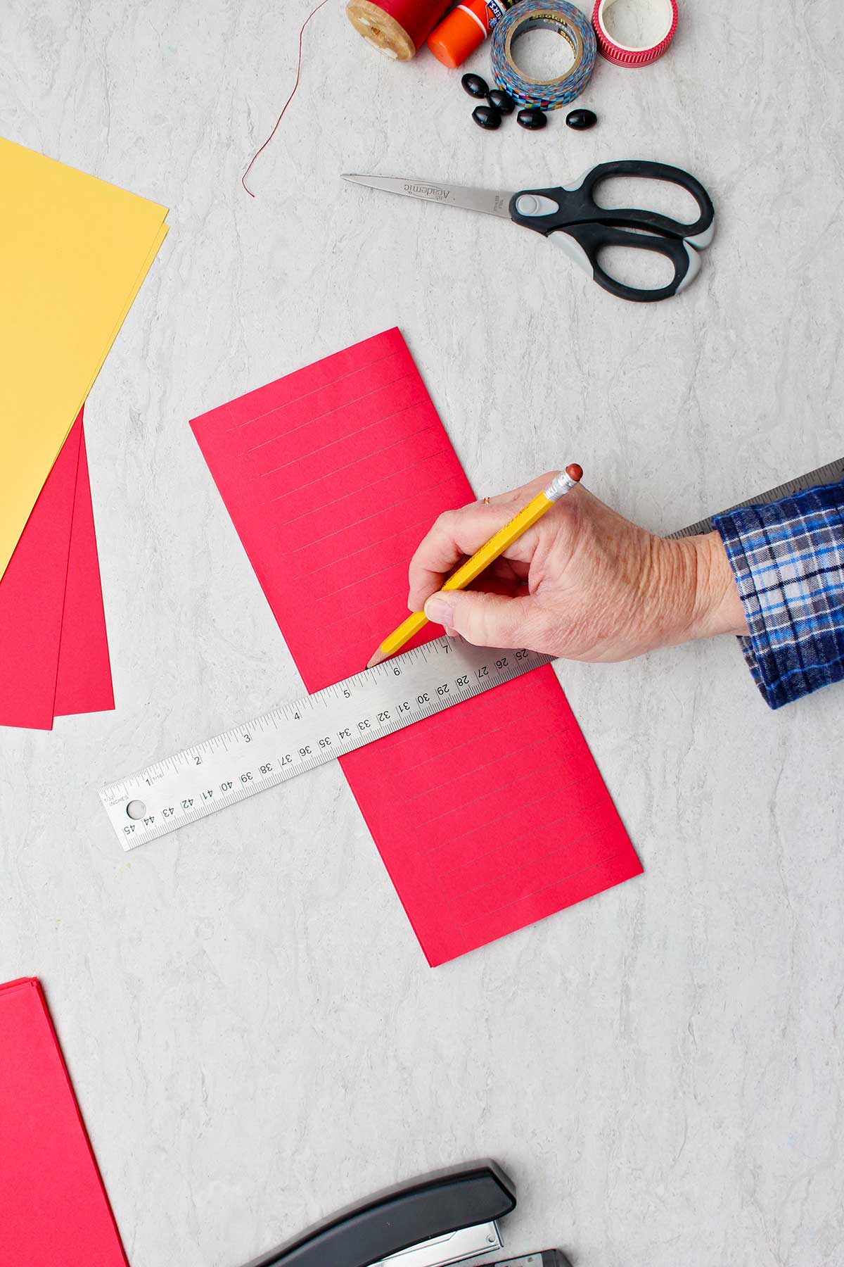 Desenhando linhas à mão com lápis em papel vermelho dobrado para fazer a base da lanterna.