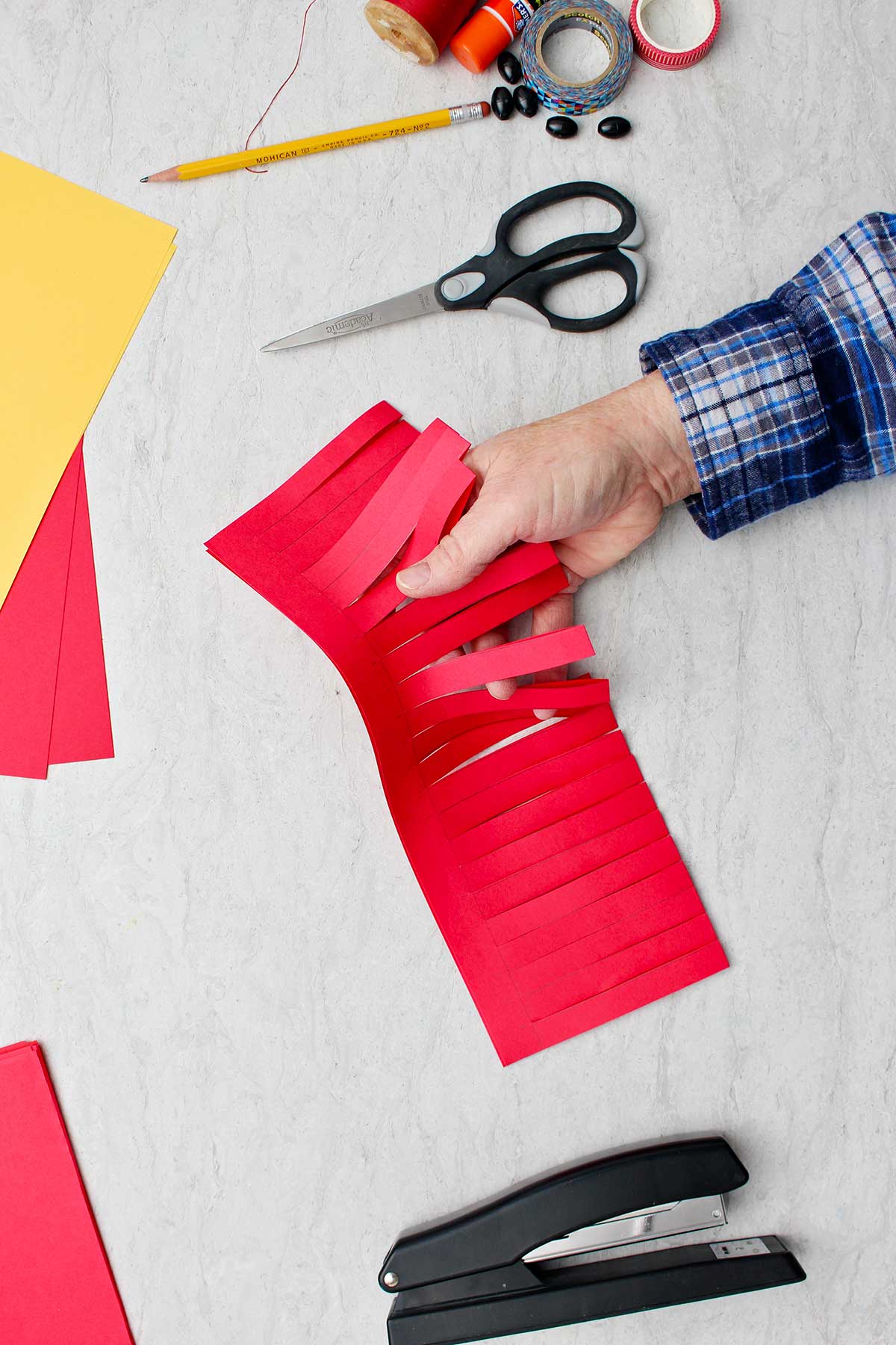 Mão mostrando pedaço de papel vermelho dobrado com tiras cortadas parcialmente para fazer a base da lanterna.