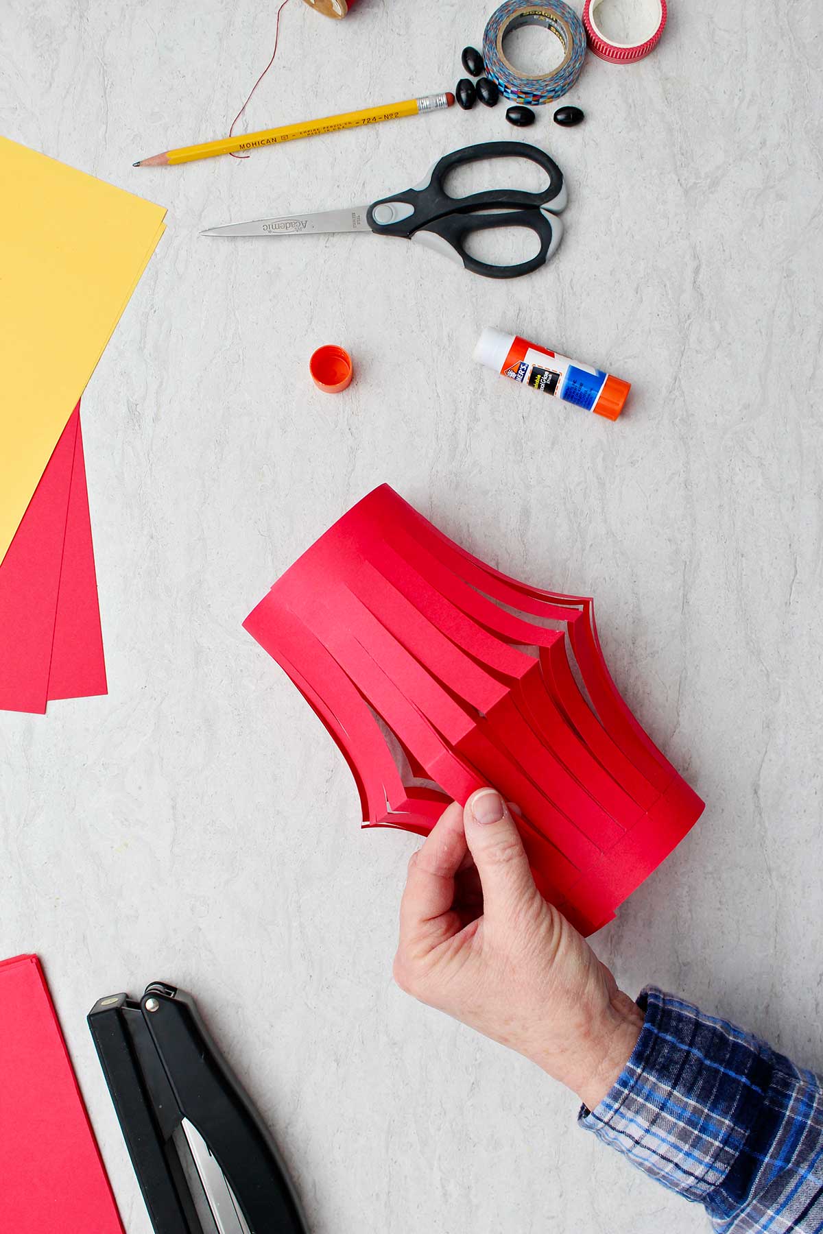 Mão mostrando a base da lanterna de papel vermelho com suprimentos ao redor.