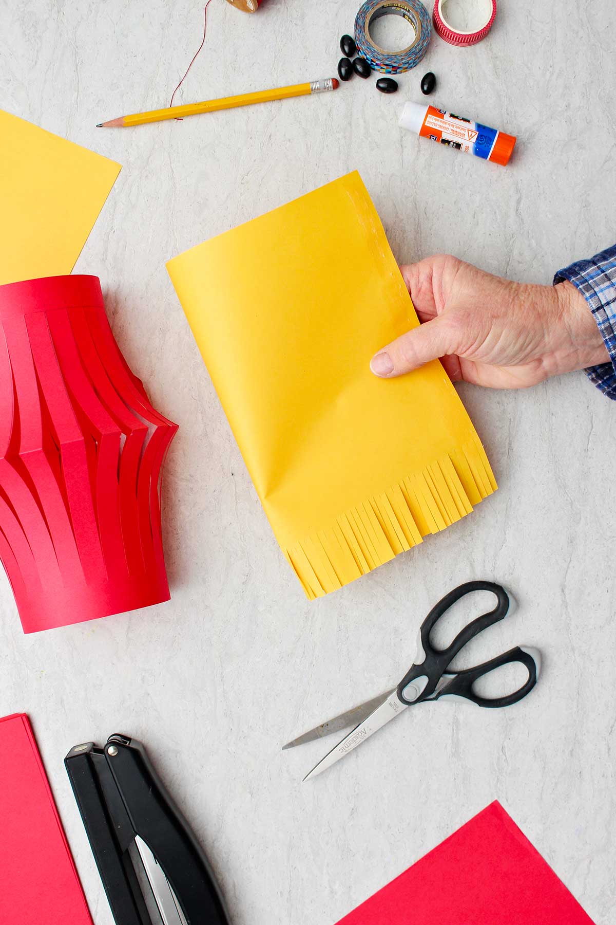 Mão mostrando um pedaço de papel amarelo com a parte inferior cortada em formato de franja.
