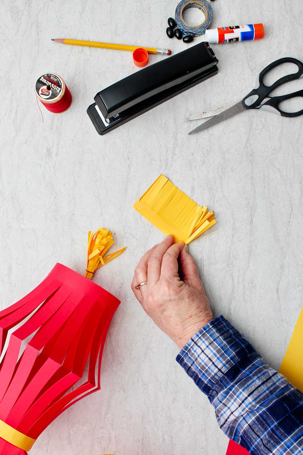 Mão dobrando a franja feita de papel amarelo cortado com suprimentos ao redor.