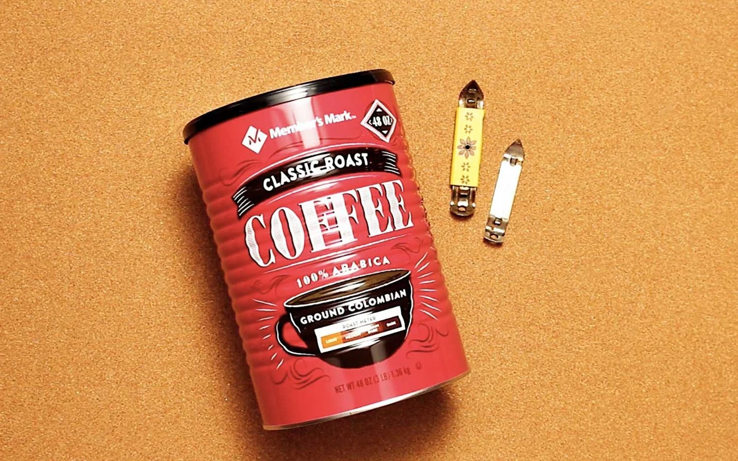 Dois pequenos abridores de lata e uma lata de café descansando sobre um fundo cor de cortiça.