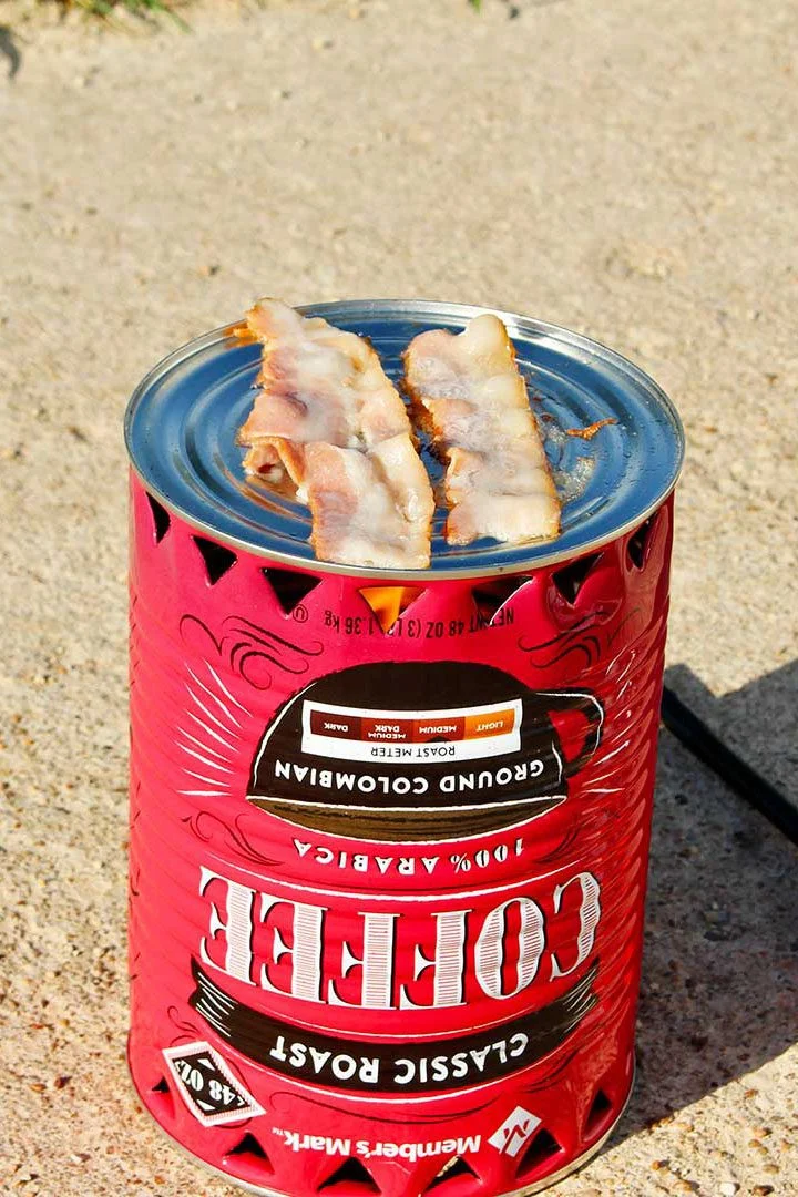 Pedaços de bacon prestes a serem cozidos em um fogareiro de pobre com um isqueiro laranja descansando na entrada da garagem.