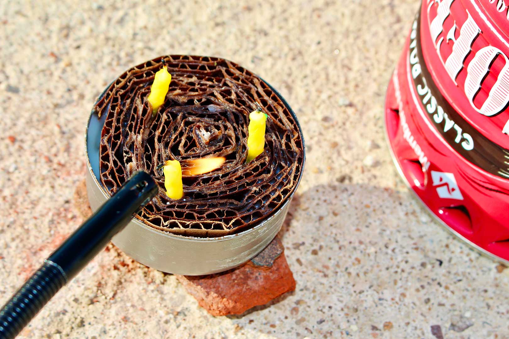 Alguém acendendo pequenas velas amarelas no buddy burner de um fogareiro de pobre.