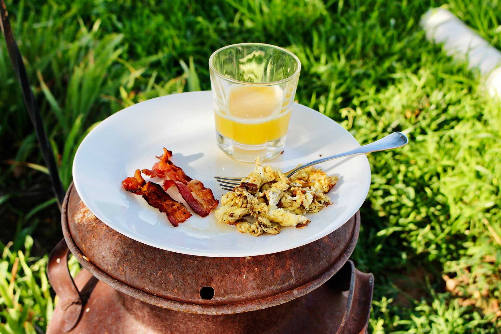 Um prato de bacon, ovos e suco no café da manhã sentado em cima de uma lata de óleo velha.