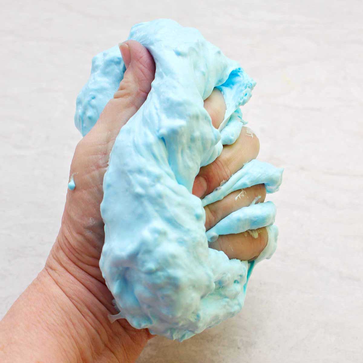 Mão apertando um lote pronto de slime fofo azul claro.