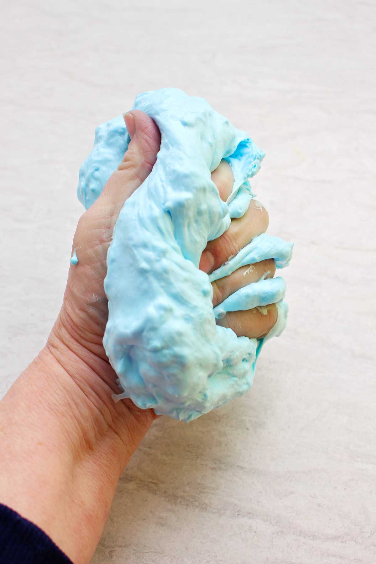 Mão espremendo um lote completo de slime fofinho de cor azul clara.
