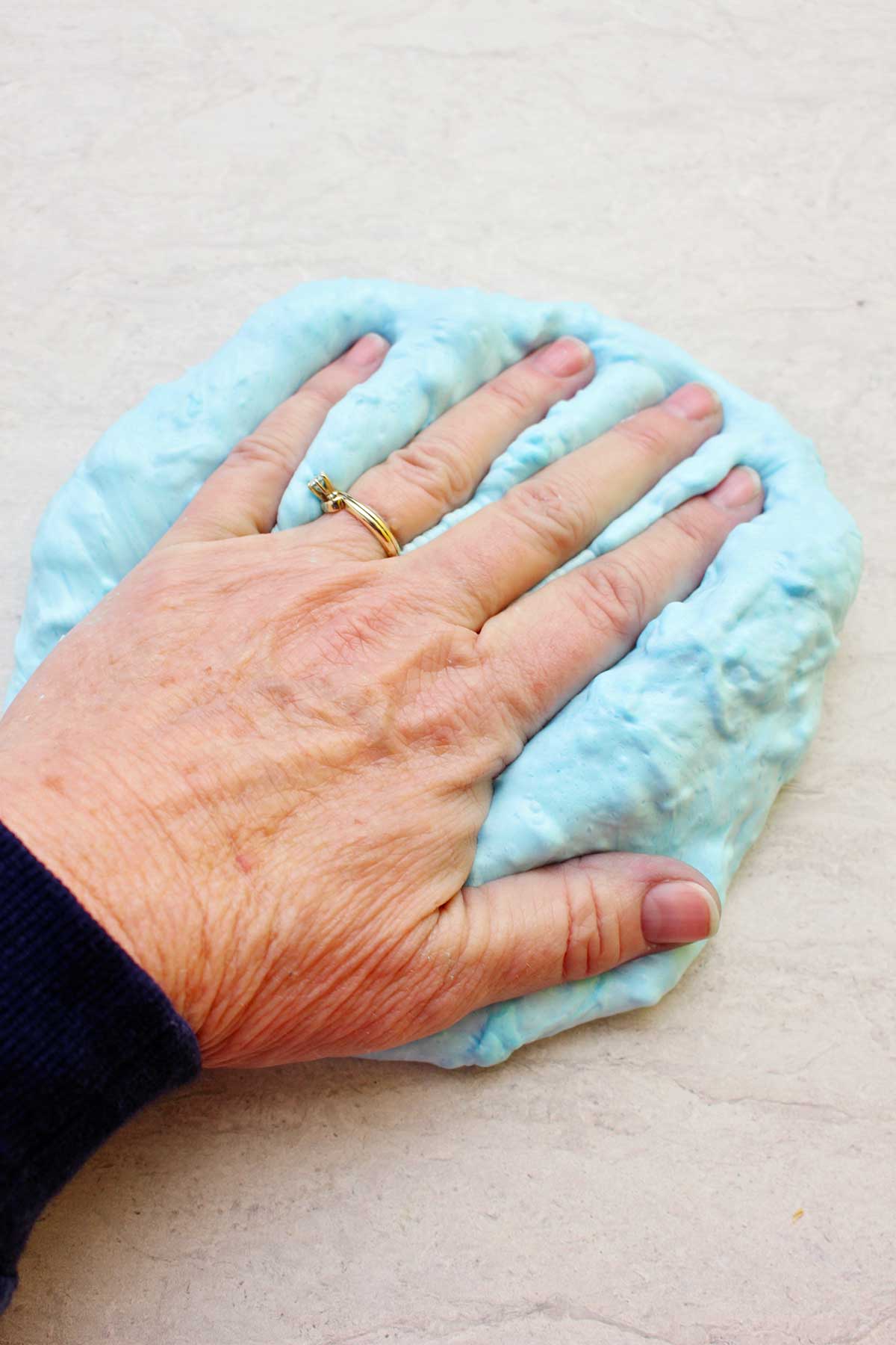Mão pressionando uma porção de slime fofa azul clara já finalizada.